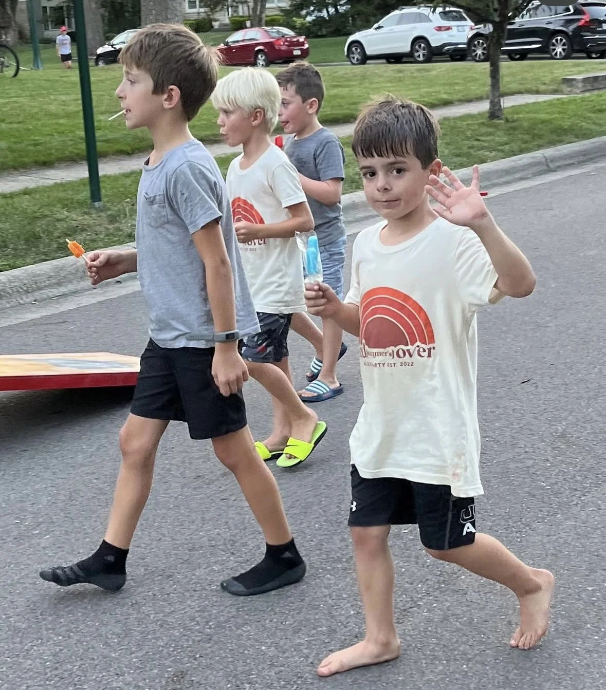 Kids waving while walking down street wearing custom annual neighborhood party shirts.