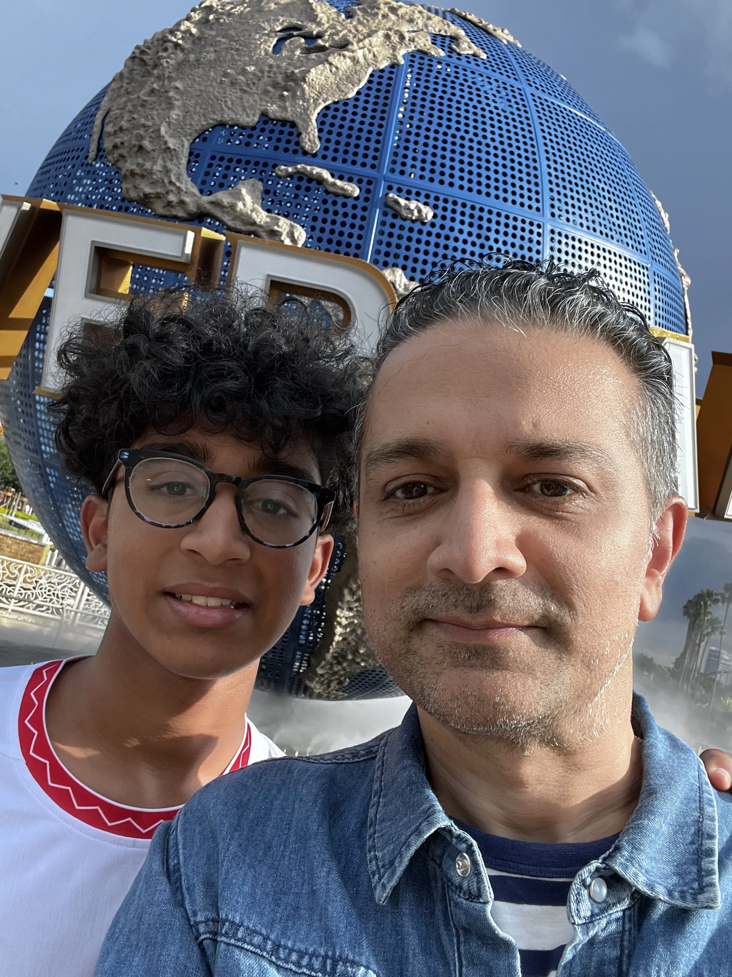 Alok Dube, MD, integrative psychiatrist and his son taking a selfie in front of the Universal Studios globe at Universal Studios theme park.