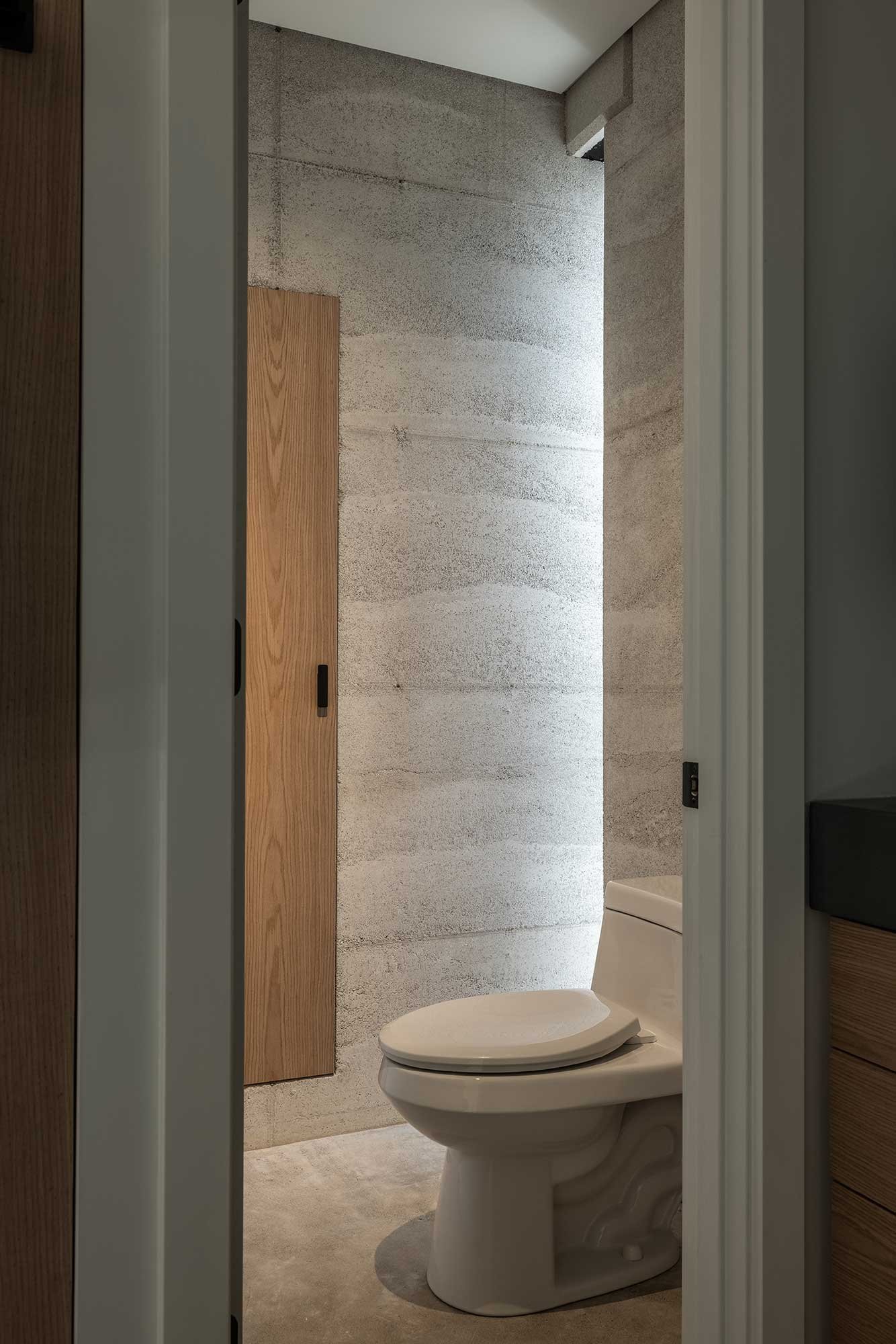 Bathroom with clean white fixtures and built in cabinetry framed by Rammed Earth walls.
