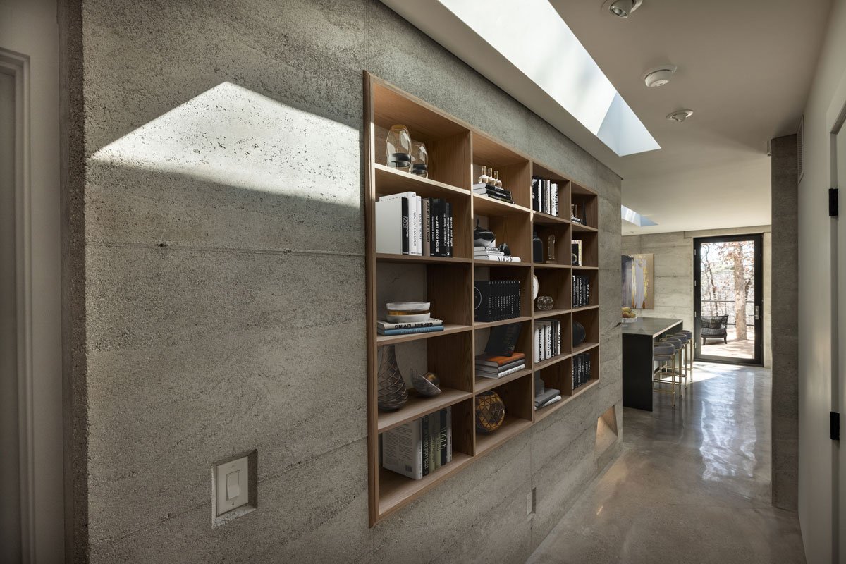 Hallway lined with built-in bookshelf carved into Rammed Earth wall.