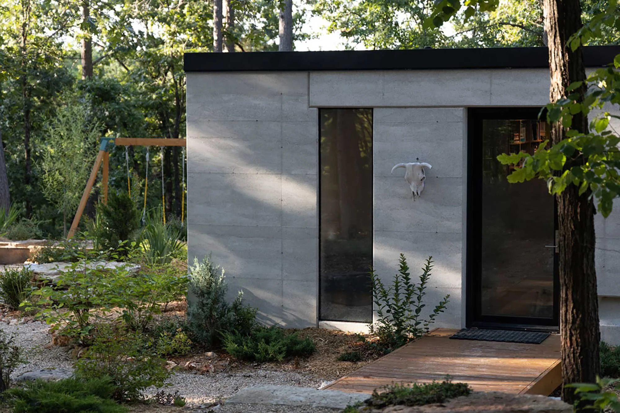 Wide shot of CALX Cabin nestled among trees with Rammed Earth walls.