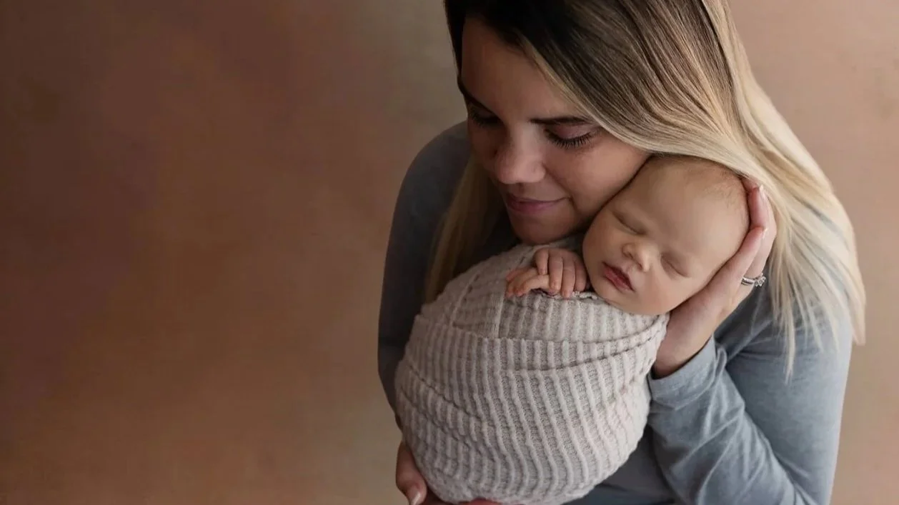 A woman holding a sleeping baby wrapped in a beige blanket close to her face