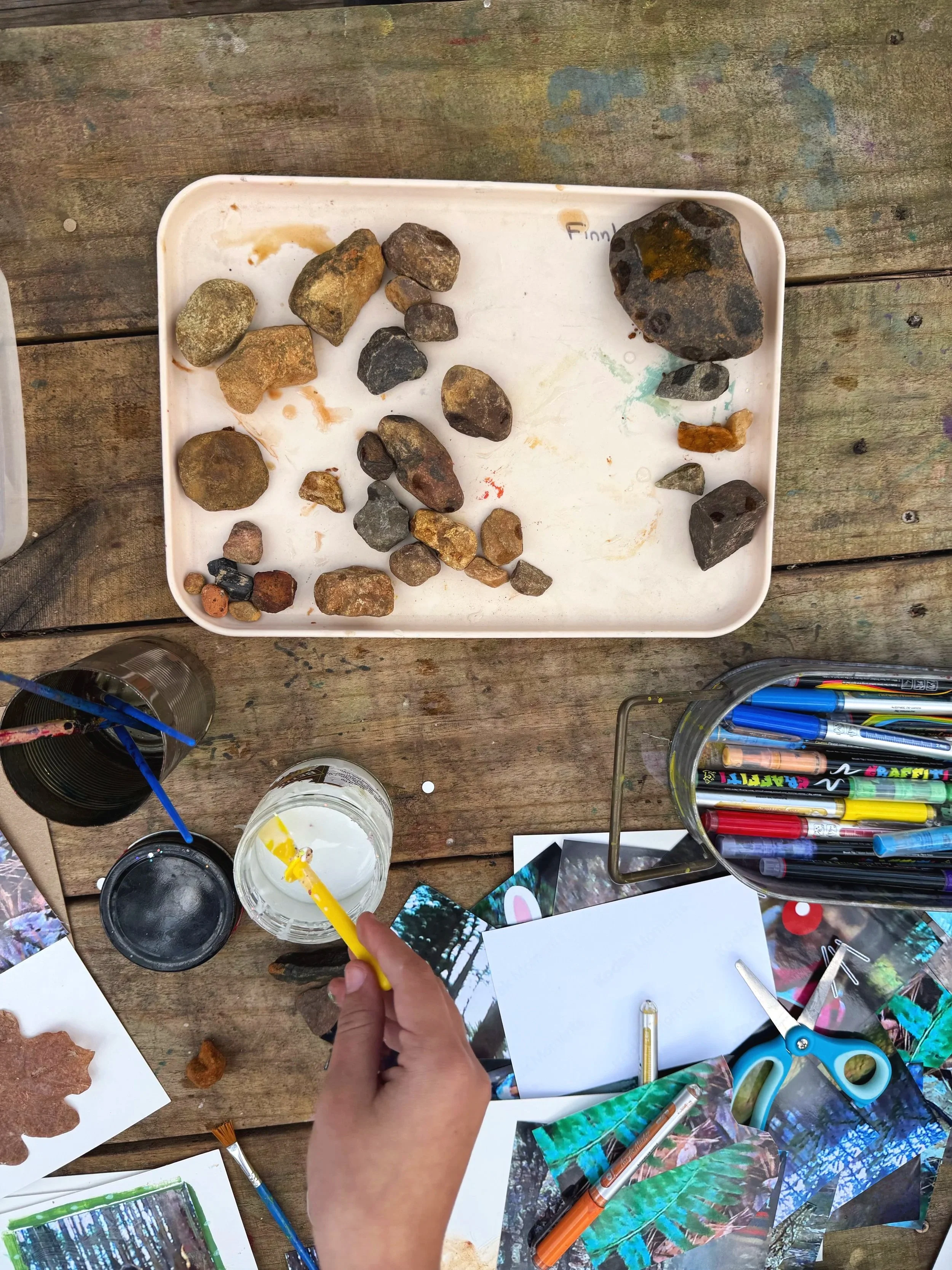 Kids working on nature journal craft project with photos, markers, glue, and natural pigment paint rocks.
