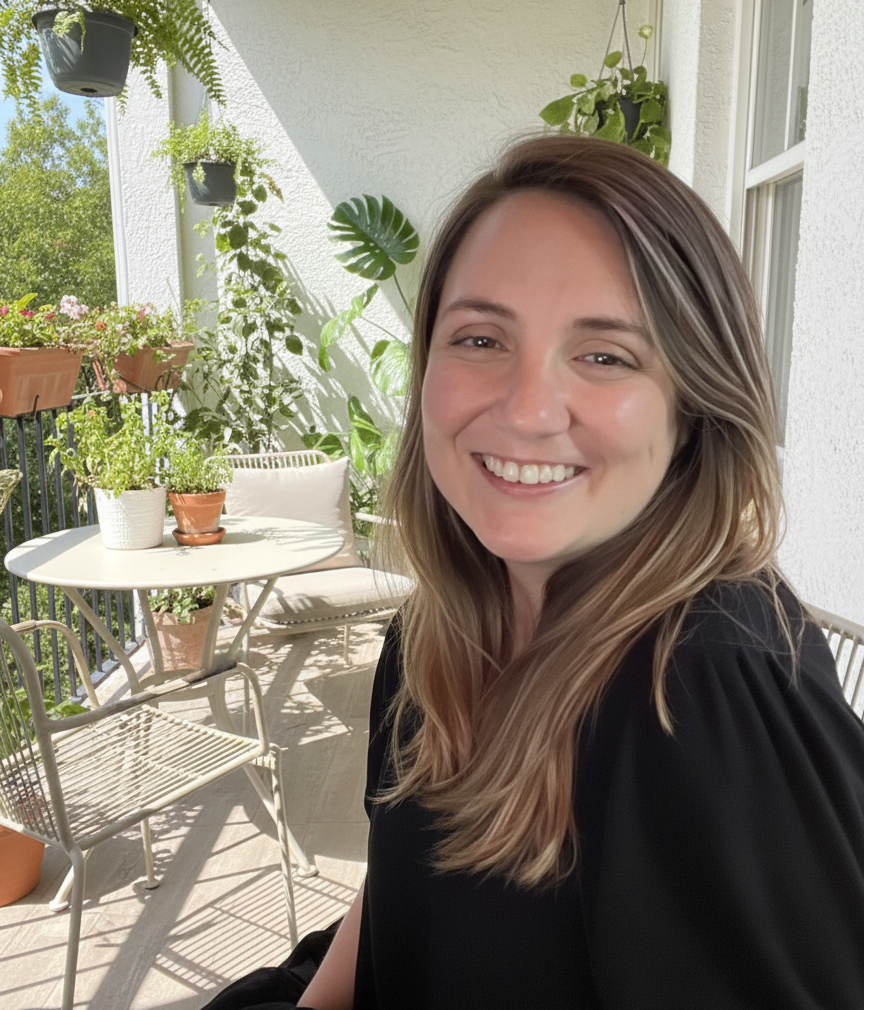 A woman smiling on a balcony with potted plants and greenery, sunshine, and outdoor furniture.