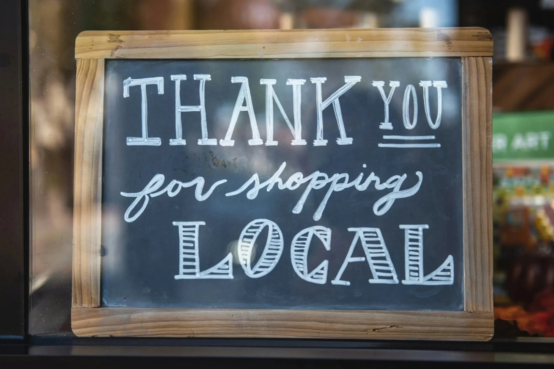 A chalkboard sign with a wooden frame that says, 'Thank you for shopping local' in white handwritten letters.