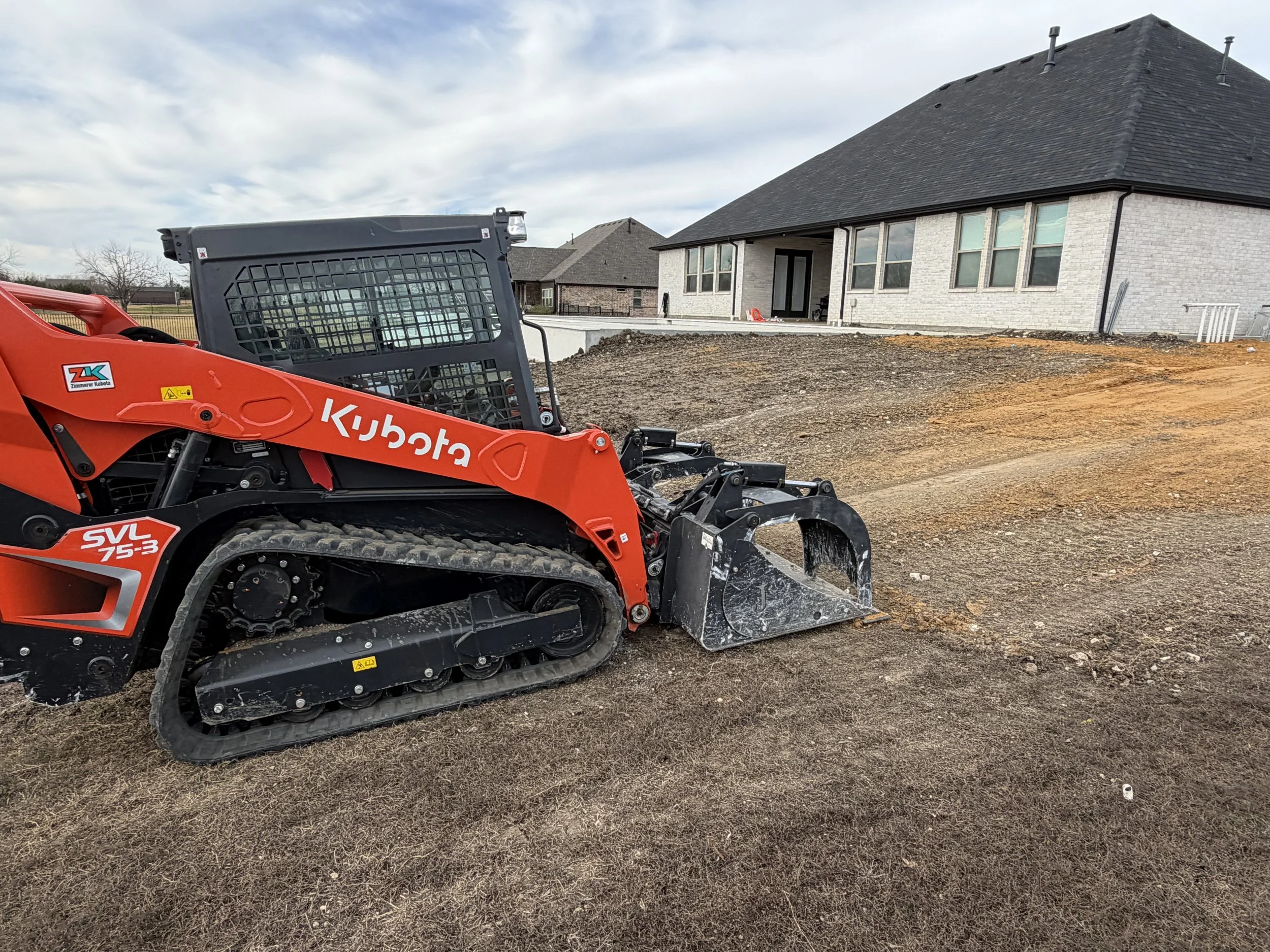 A bulldozer grading a dirt area with tire tracks, surrounded by grass, trees, and a partly cloudy sky.