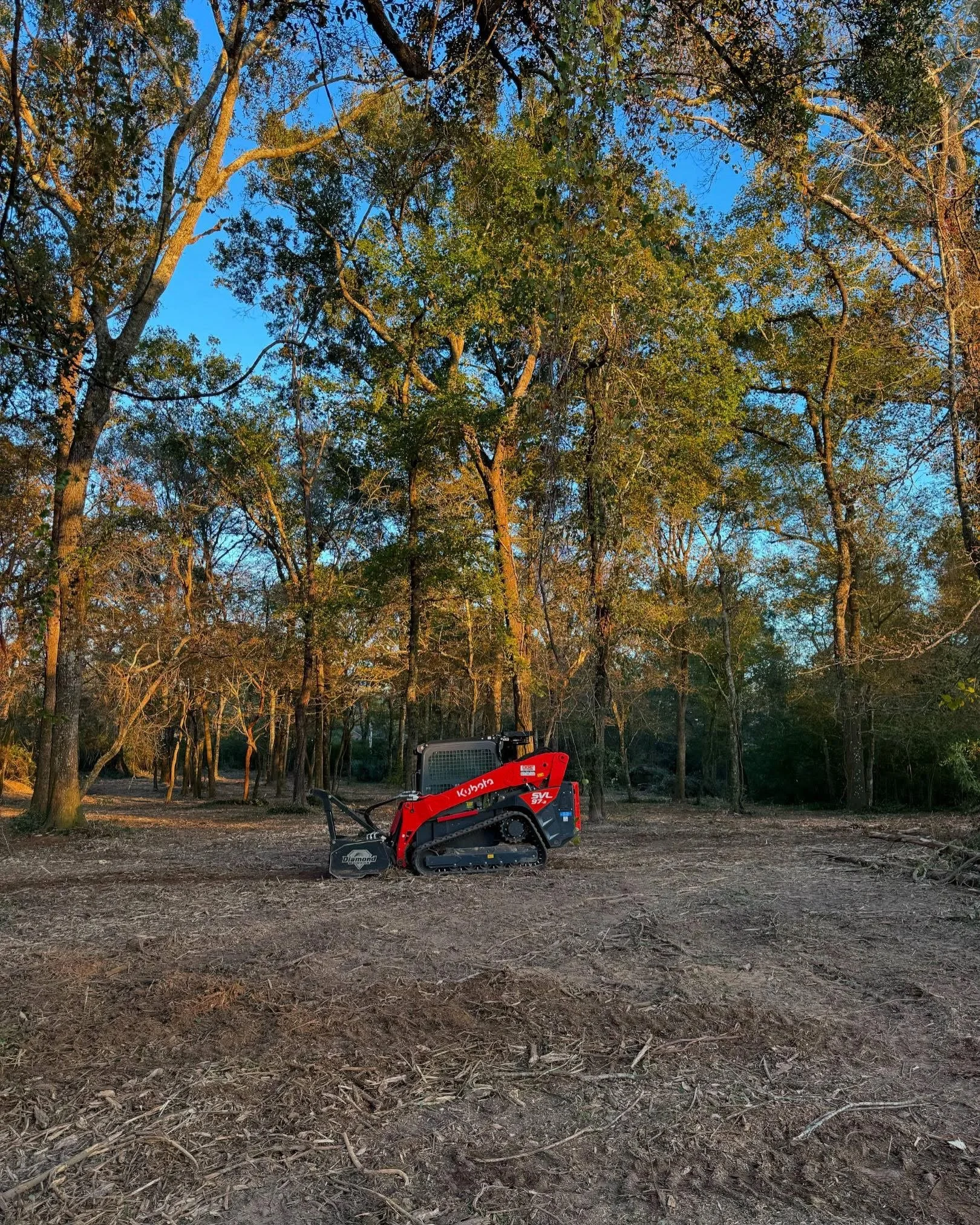 A bulldozer working on a dirt slope in a rural area with green trees and grass.