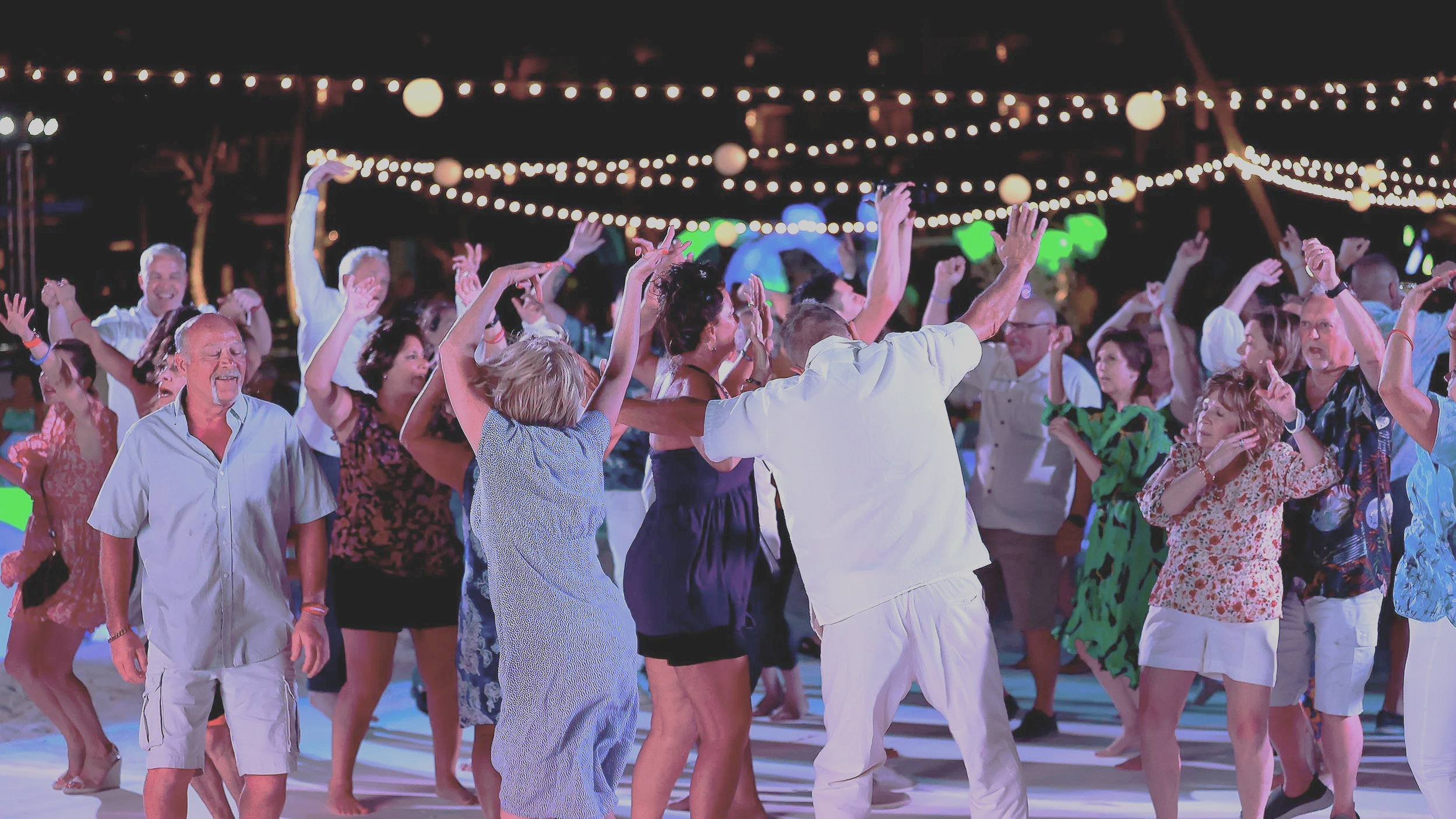 People dancing at a lively outdoor wedding party at night, decorated with string lights and paper lanterns.