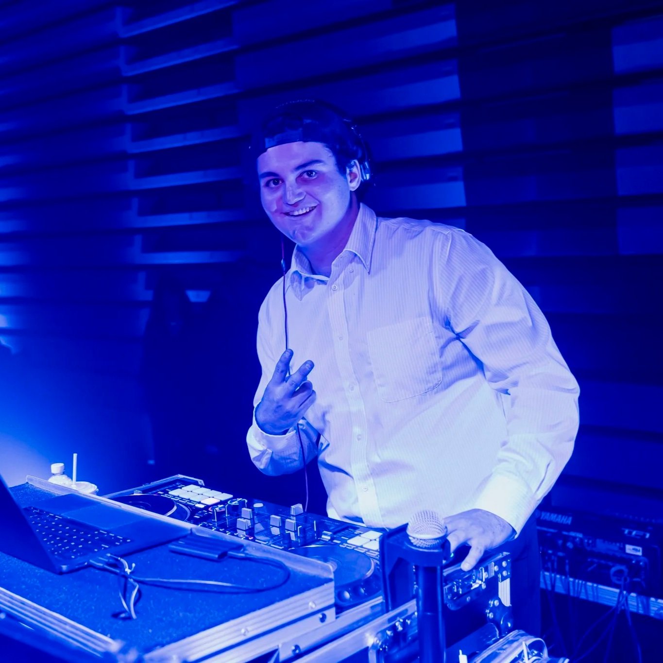 DJ smiling at a music mixing console with a blue lighting background.