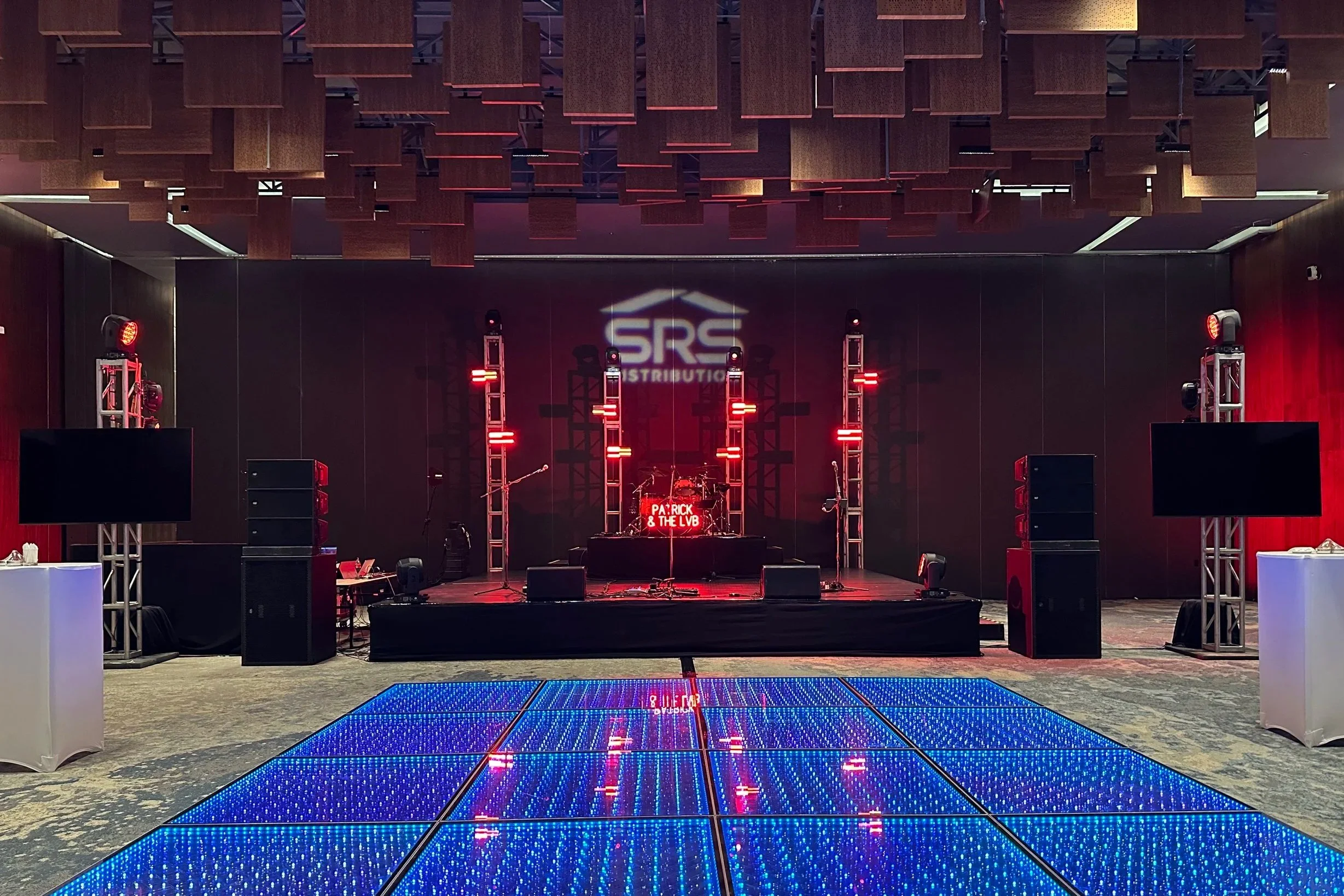 Event stage with LED lights, speakers, and musical instruments, with a blue illuminated dance floor in the foreground.