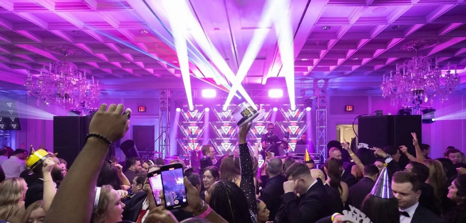 People celebrating at a party with purple lighting, wearing party hats, and a live band performing on stage