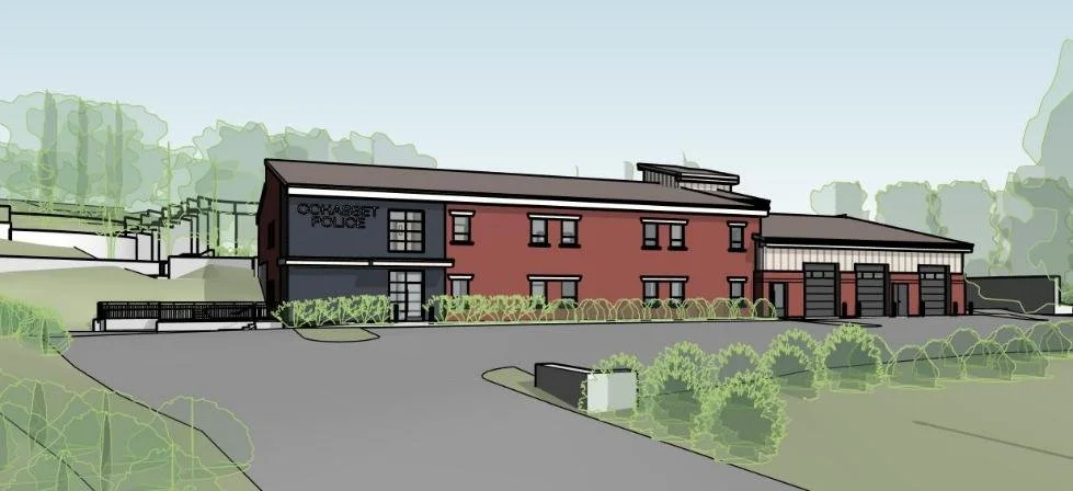 Illustration of a modern police station with a red brick facade, multiple garage entrances, landscaped surroundings, and a sloped driveway.