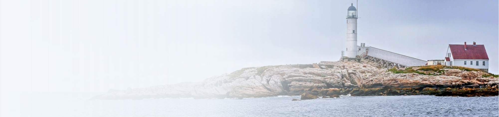 Lighthouse on rocky coast with a small white house nearby, under cloudy sky.