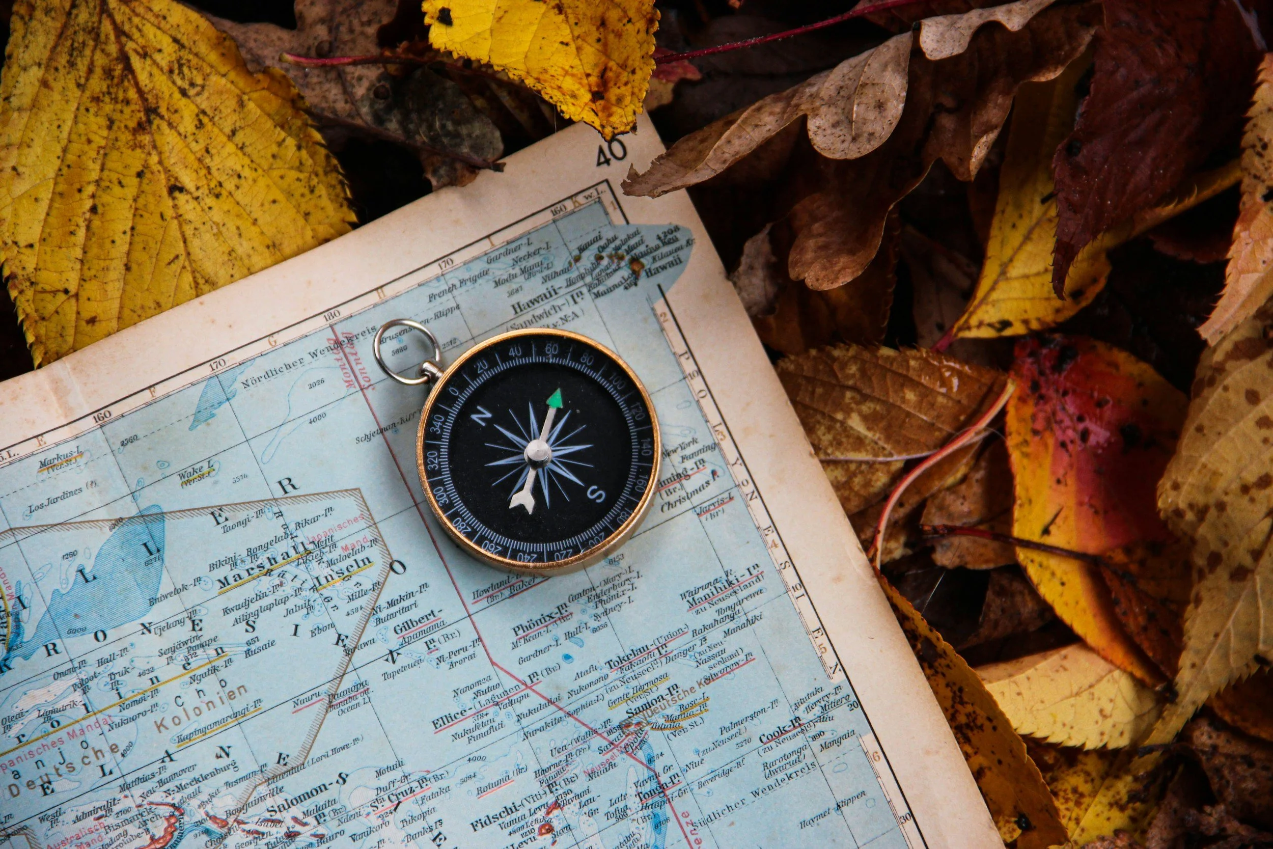 A compass resting on a map of Hawaii, surrounded by autumn leaves.