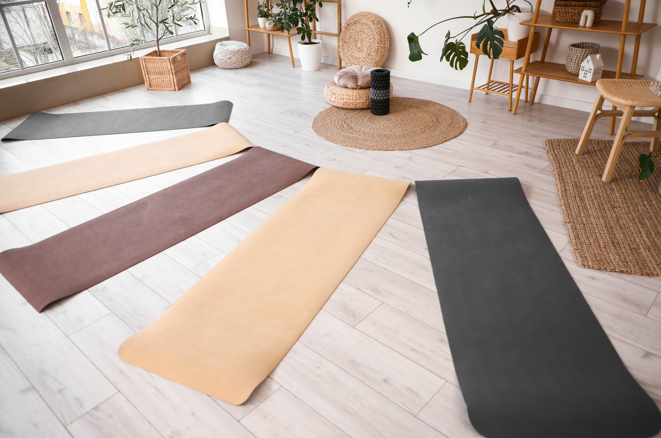 Yoga-mattor i olika färger på ett ljust trägolv i ett ljust rum med stora fönster och växter.