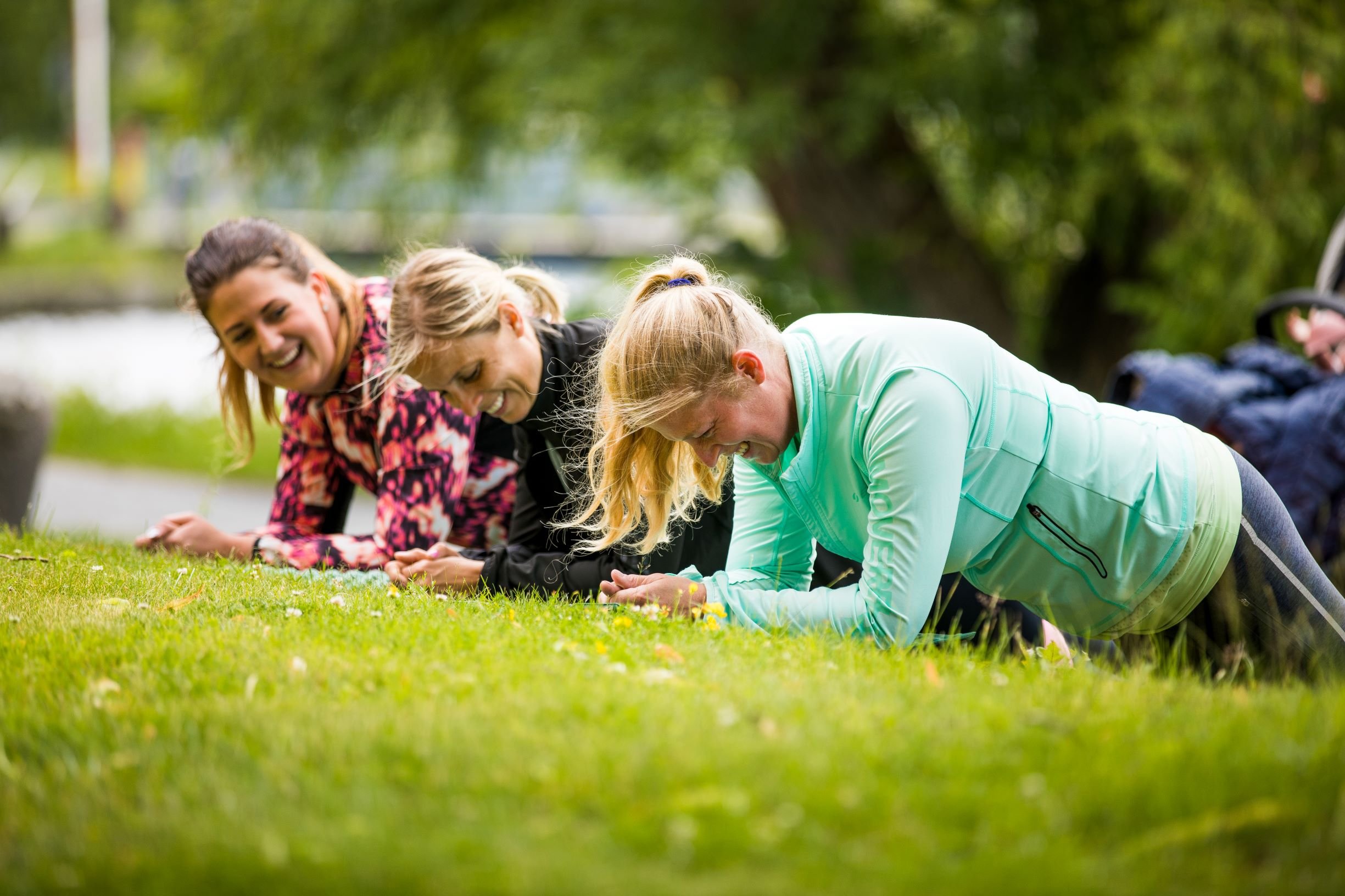 Tre kvinnor gör plankan övning på gräset i en park.
