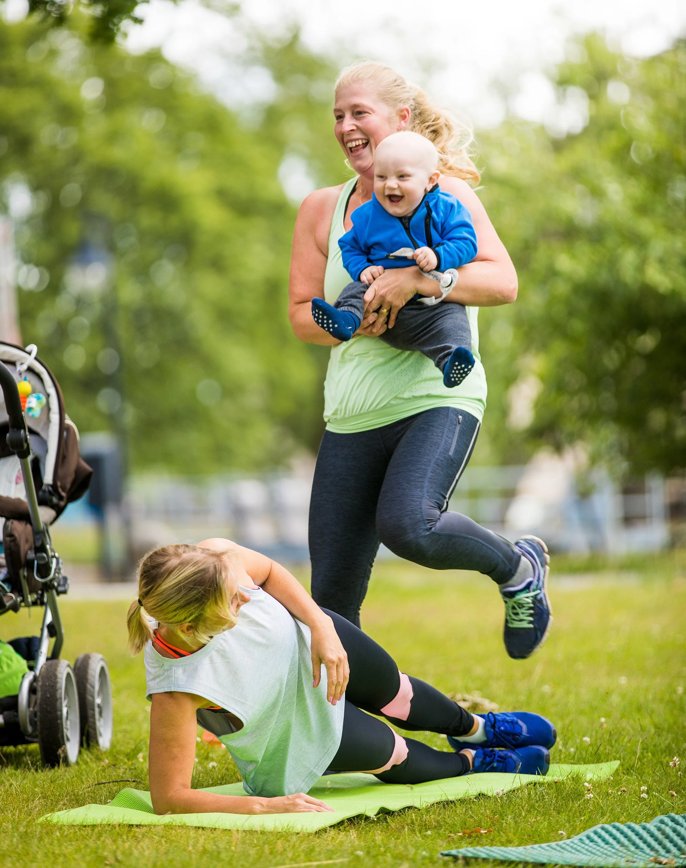 En kvinna och ett barn utomhus som tränar yoga, med barnvagn till vänster