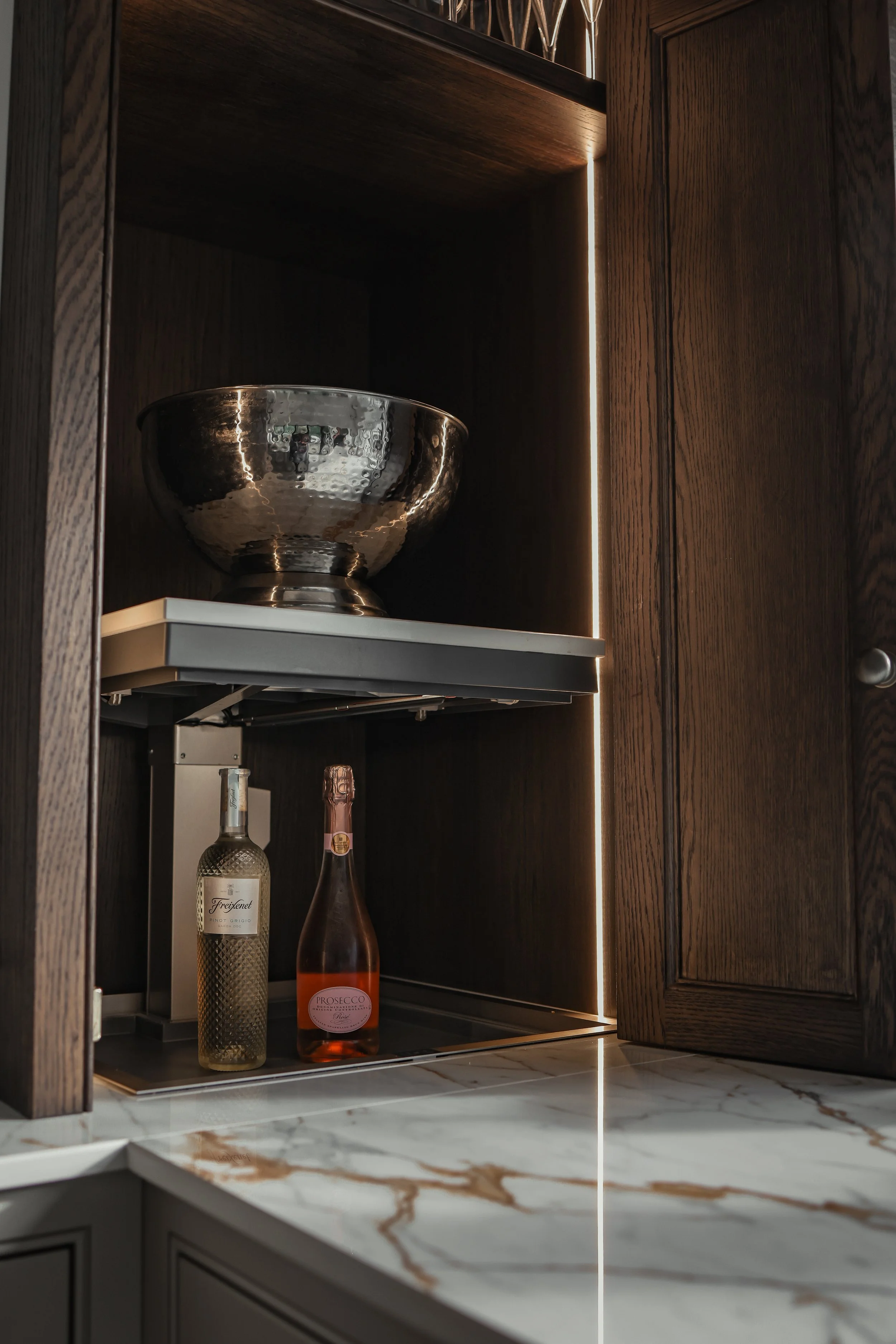 Inside a wooden cabinet containing a large metallic bowl on a shelf and two bottles of alcohol on the floor of the cabinet.