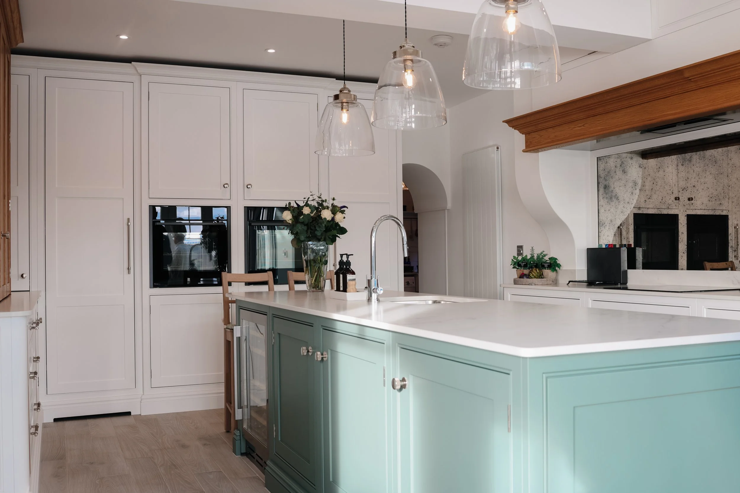 Modern kitchen with a green island, white cabinets, hanging pendant lights, and a vase of flowers on the island.