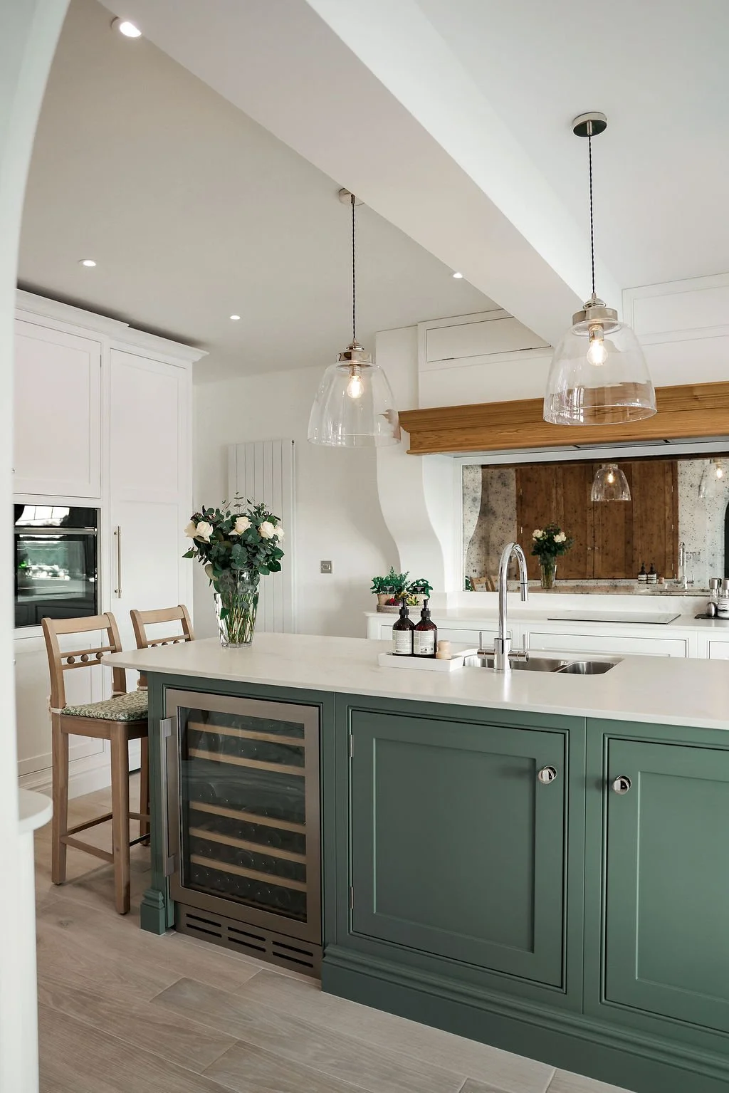 Modern kitchen with white cabinetry, a green kitchen island with a built-in wine cooler, pendant lights, and fresh flower arrangements.
