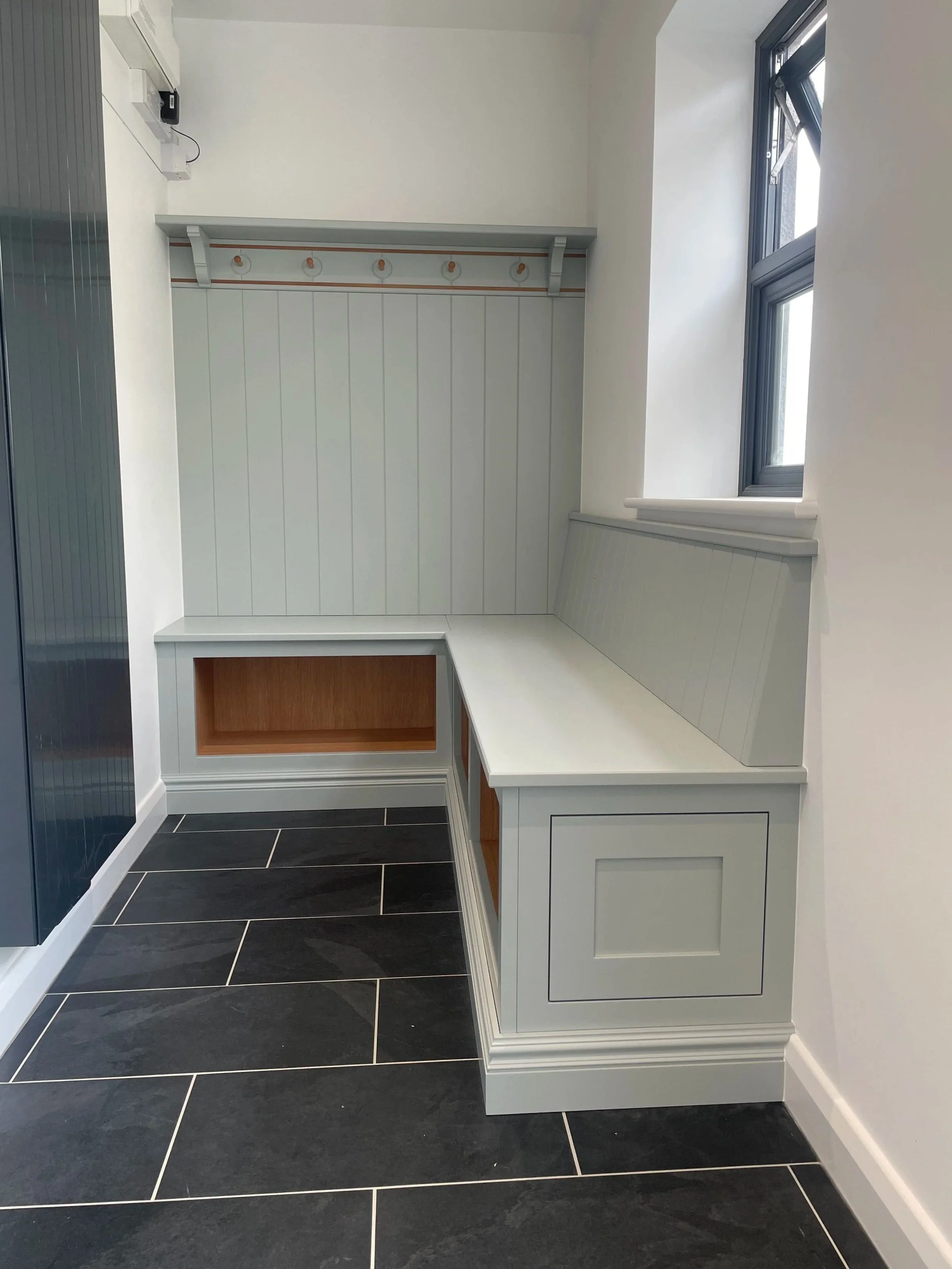 Built-in bench with storage and hooks, next to a window, in a modern kitchen or utility room.