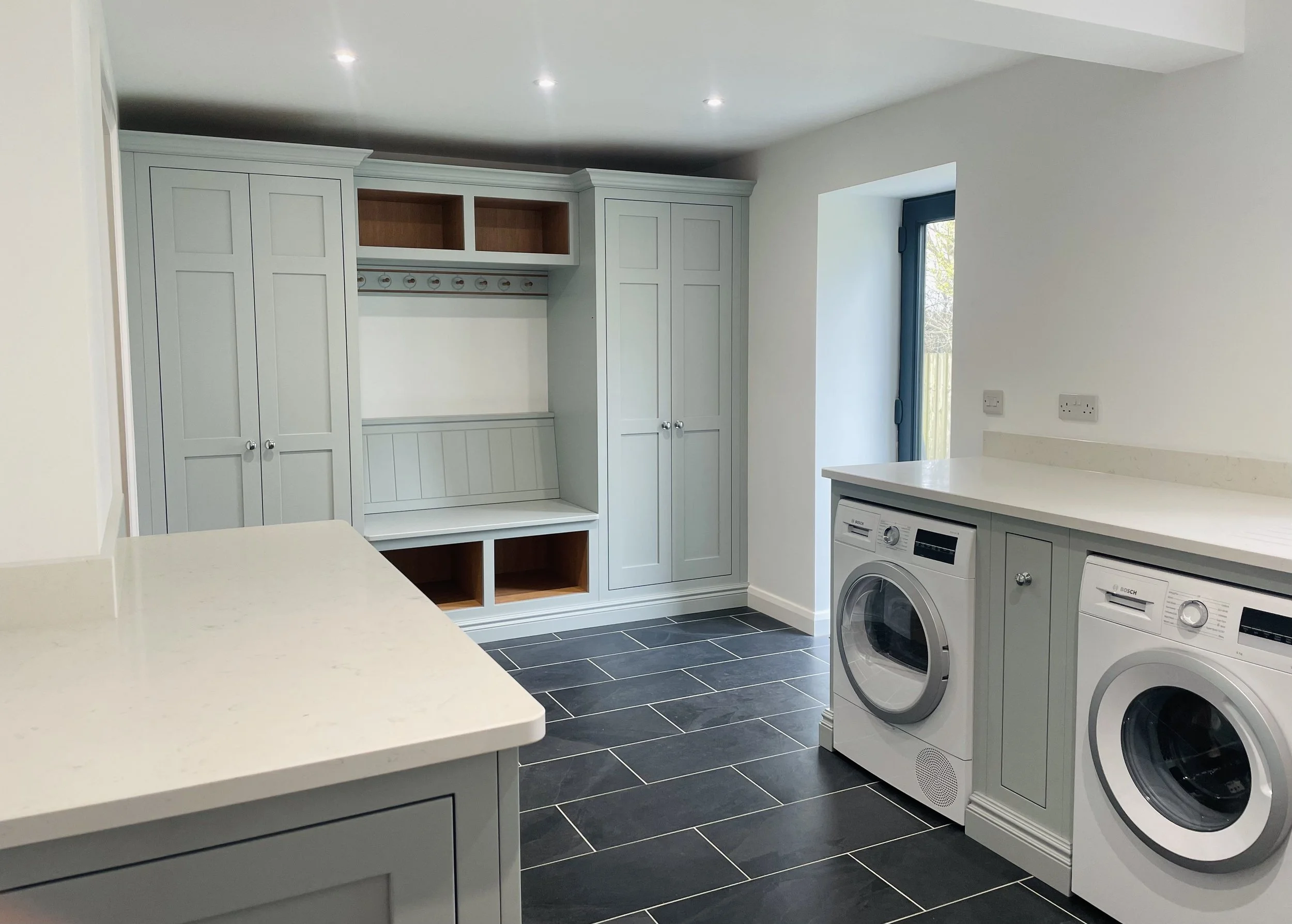 Laundry room with white cabinetry, black tile flooring, washer and dryer, white countertops, and a small window.