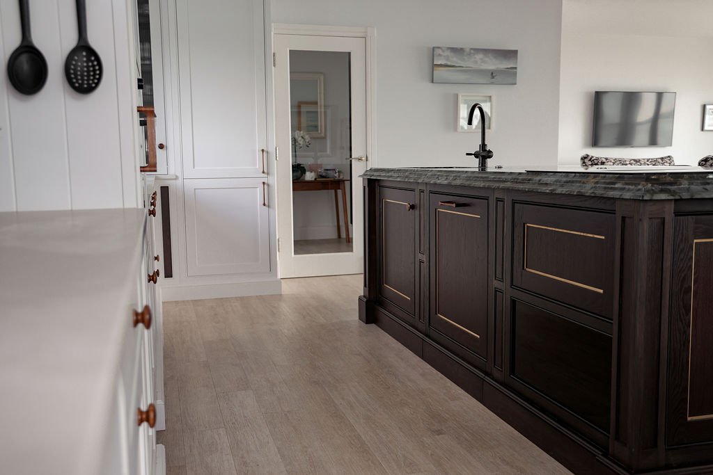 A modern kitchen with white cabinets, a dark island with a marble countertop, and a black faucet. Artwork and a TV are mounted on the wall.