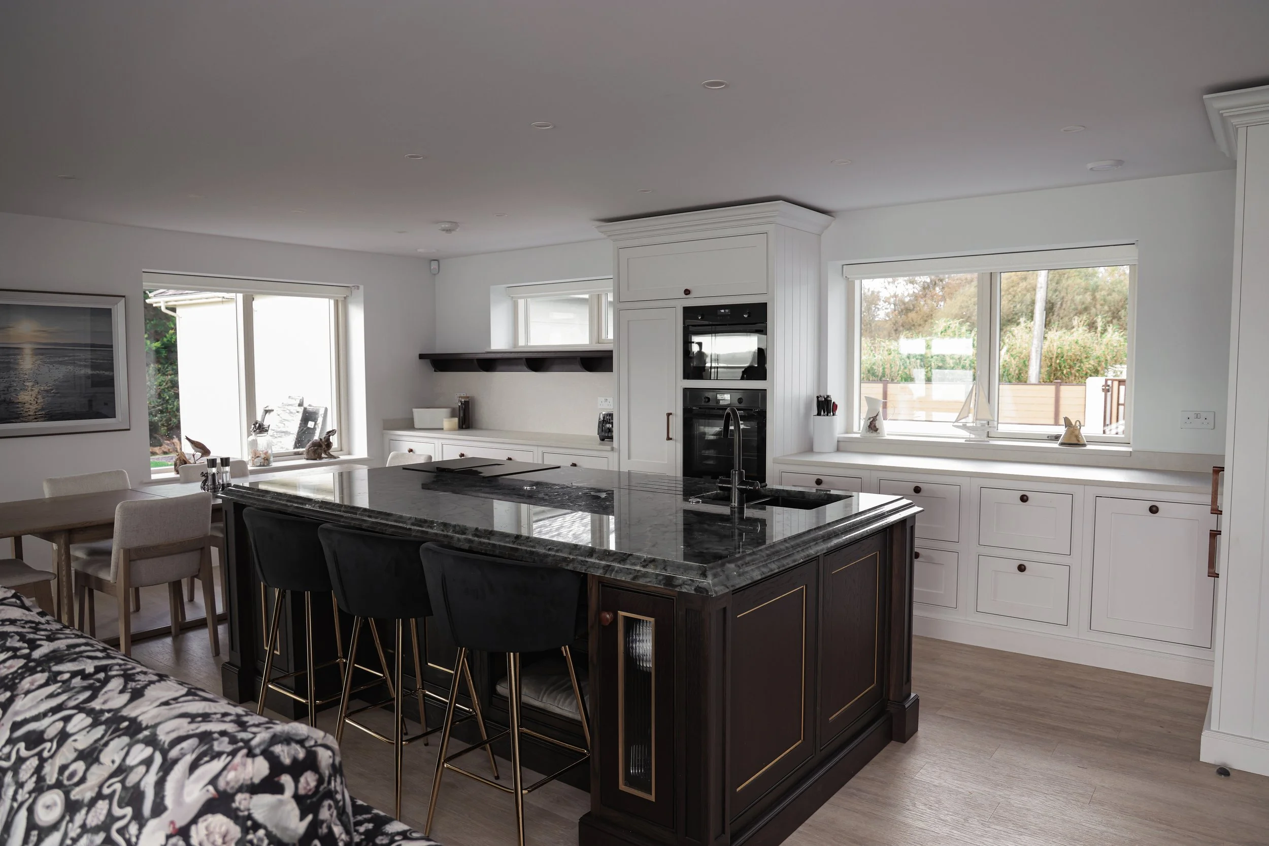 Modern kitchen with white cabinets, black island, marble countertop, and natural light from windows, with dining area nearby.