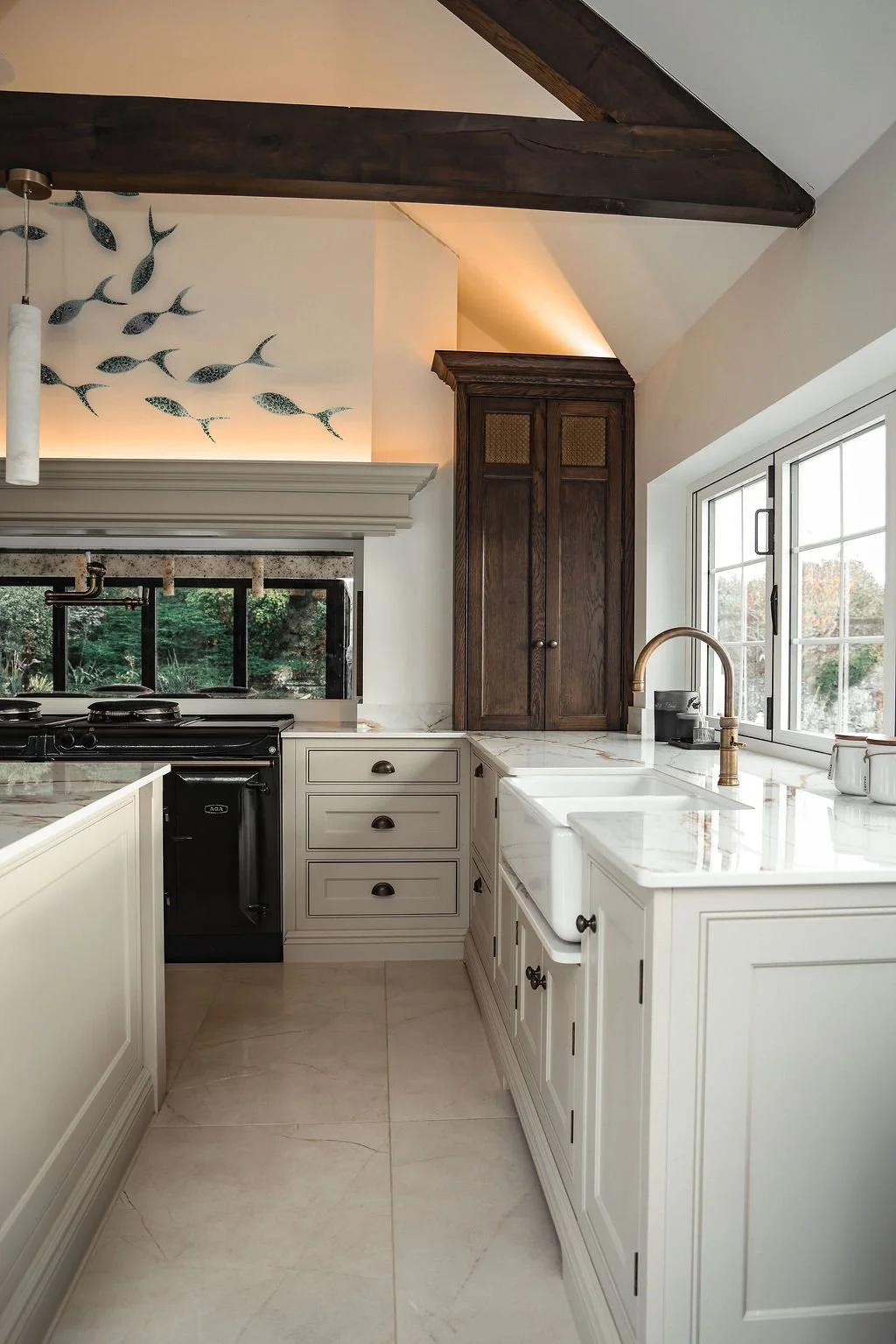 Modern kitchen with white cabinets, marble countertops, and a window overlooking a garden, with a dark wood cabinet and light fixtures.