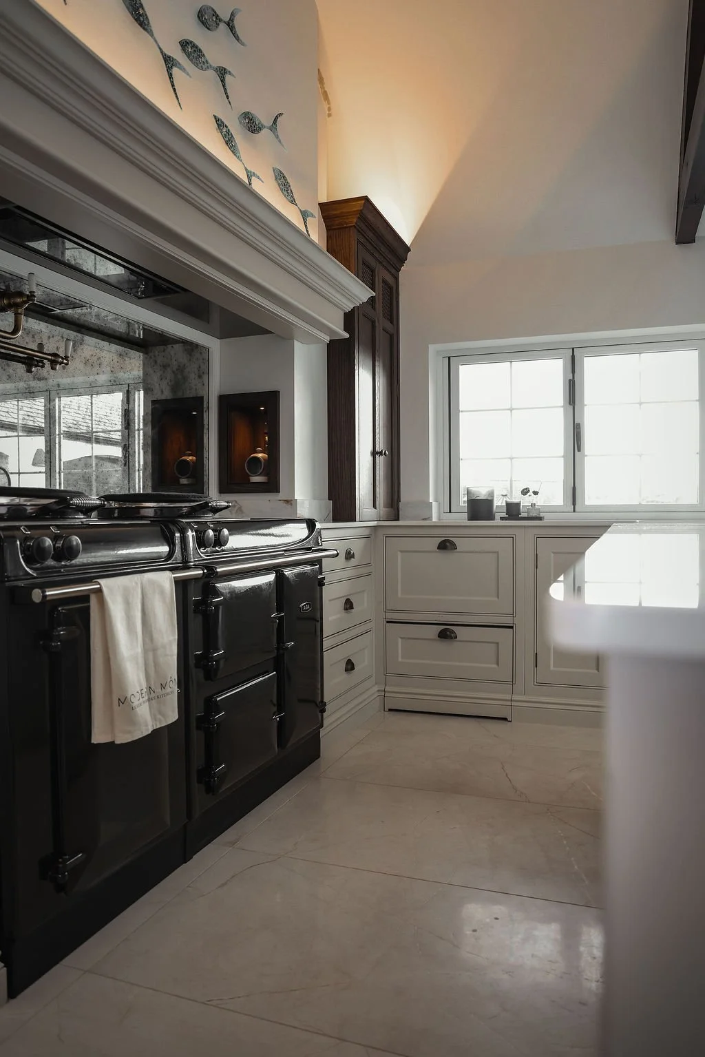 A modern kitchen with a black stove, white cabinetry, and a window allowing natural light. There are decorative fish on the wall above the stove and small items on the windowsill.
