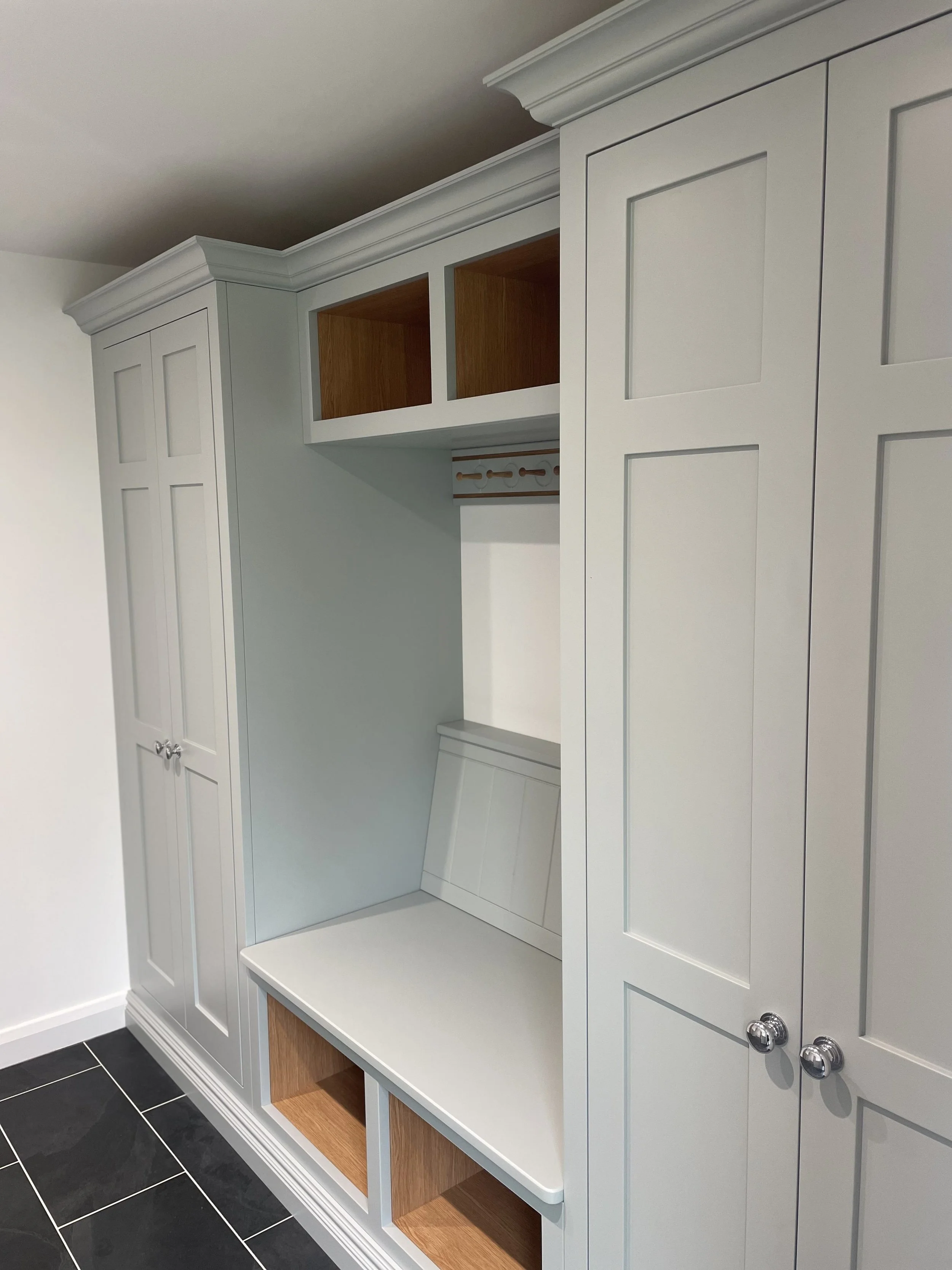 Built-in white cabinetry with closed doors, open shelving, and a bench with storage compartments, located in a modern room with black tiled flooring.