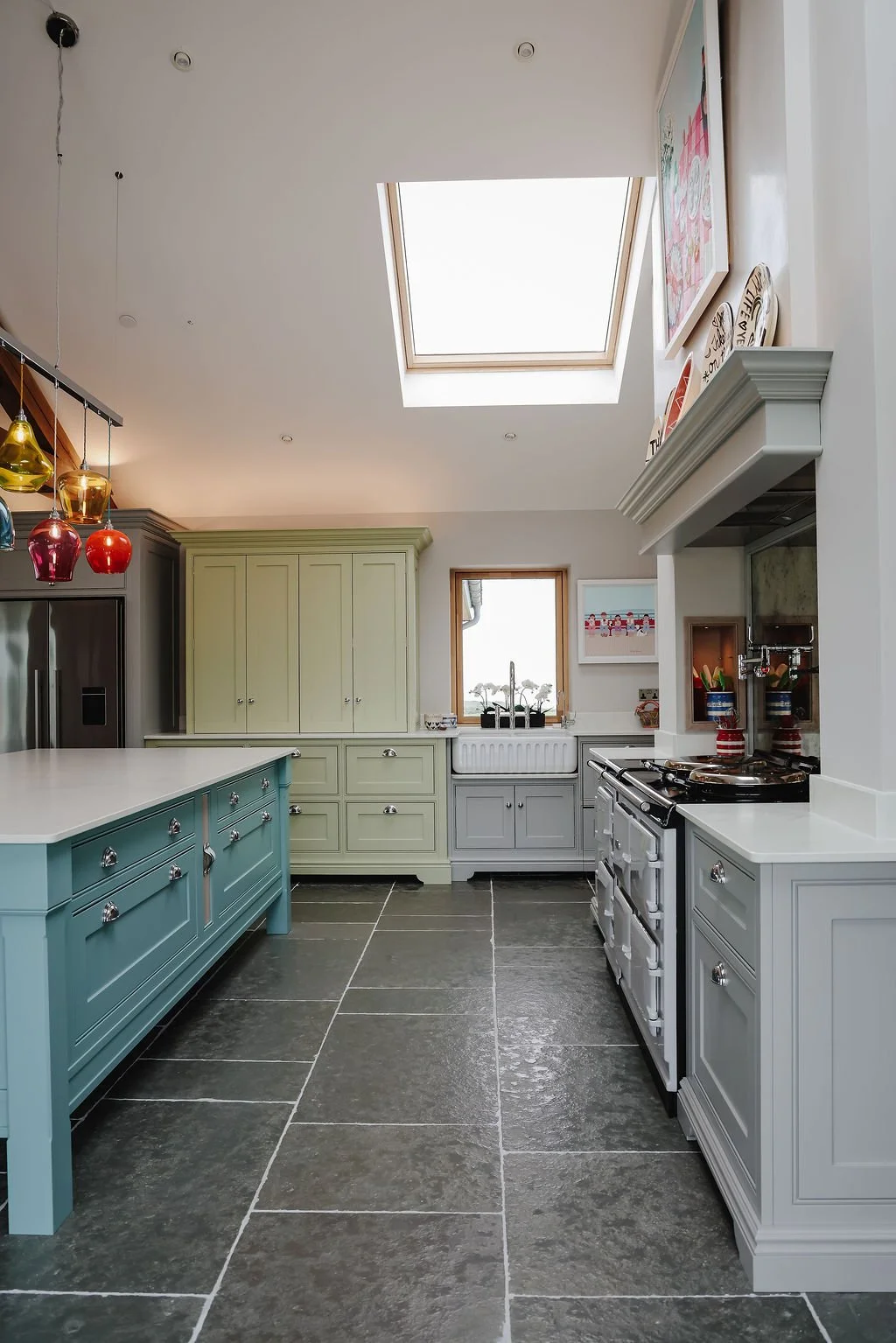 A modern kitchen with colorful cabinets and pendant lights under a skylight.