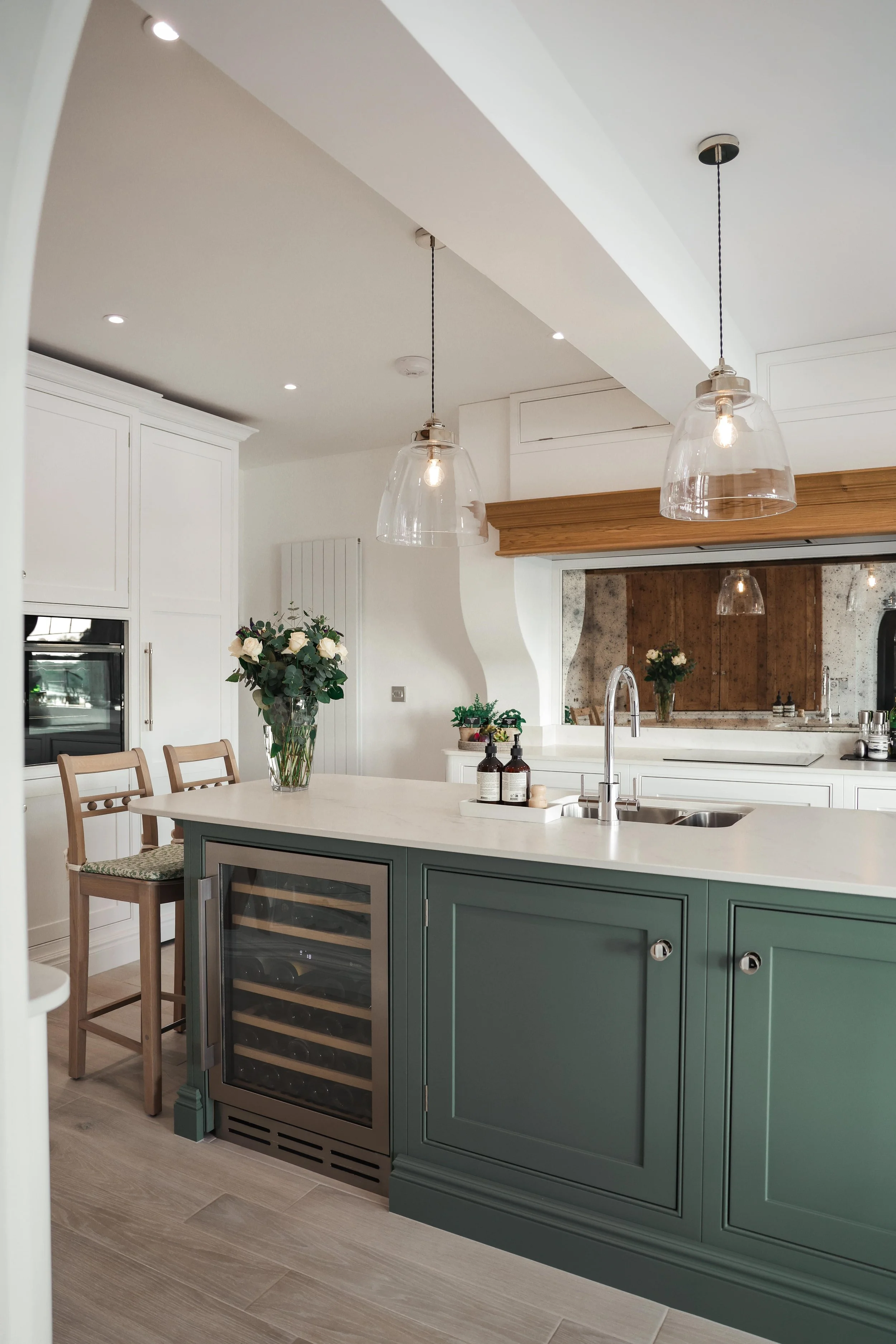 Modern kitchen with green island, white countertops, pendant lights, and wooden accents.