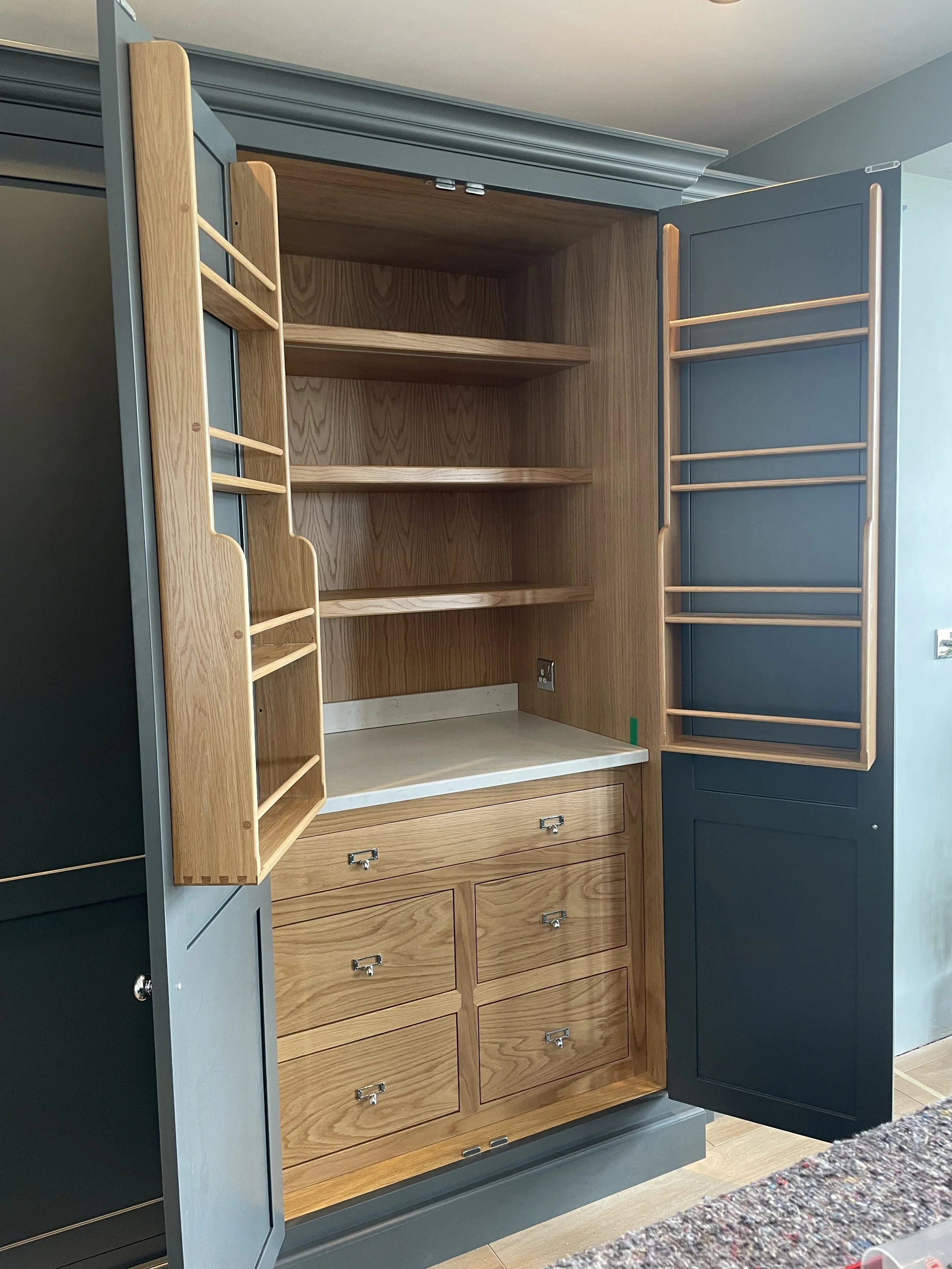 Open kitchen cabinet with wooden shelves, drawers, and side racks, painted in blue and gray colors.