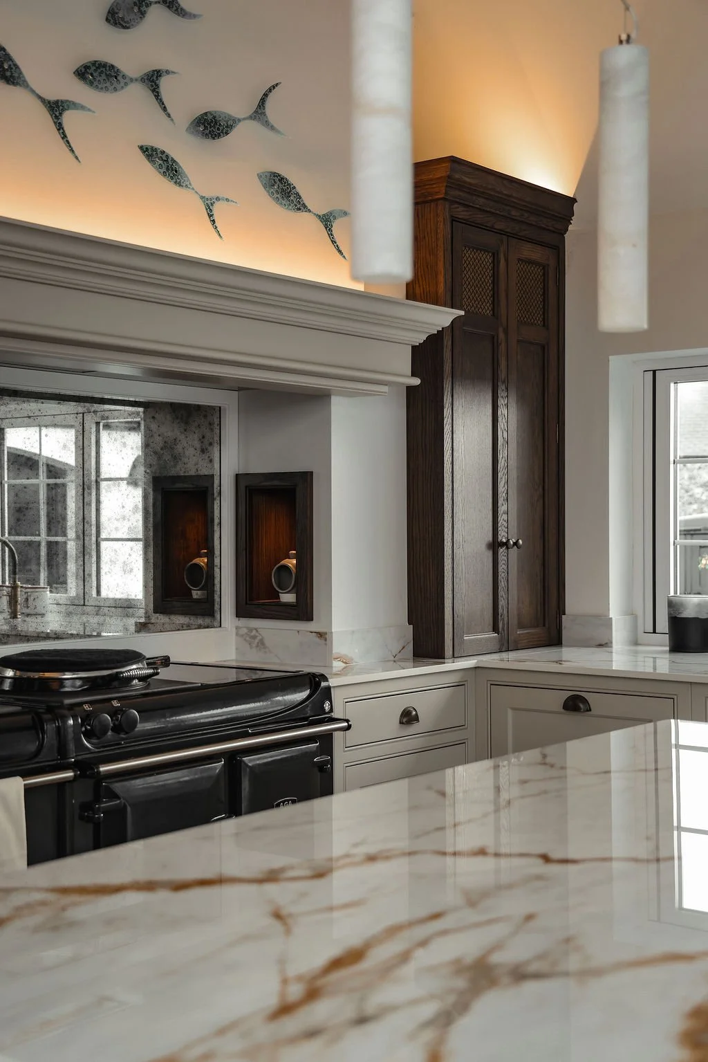 A modern kitchen with a white marble countertop, dark wooden cabinets, and a black stove. Fish decorations are mounted on the ceiling, and there are pendant lights hanging from the ceiling.