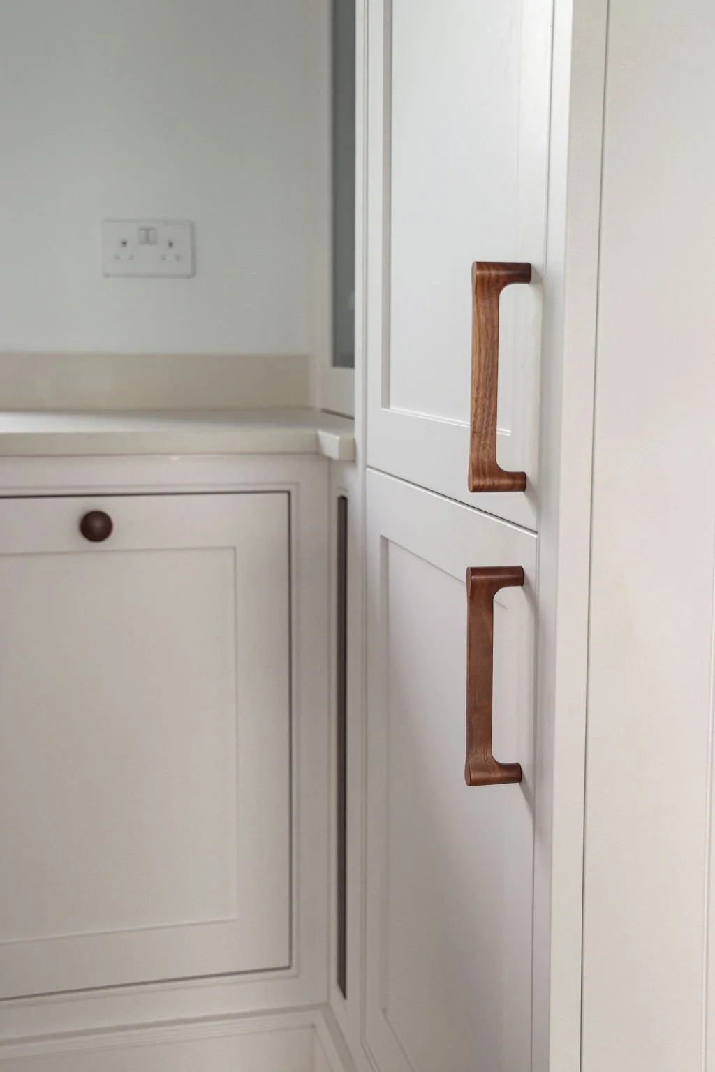Close-up of cream-colored kitchen cabinets with wooden handles and a white wall with electrical outlets.