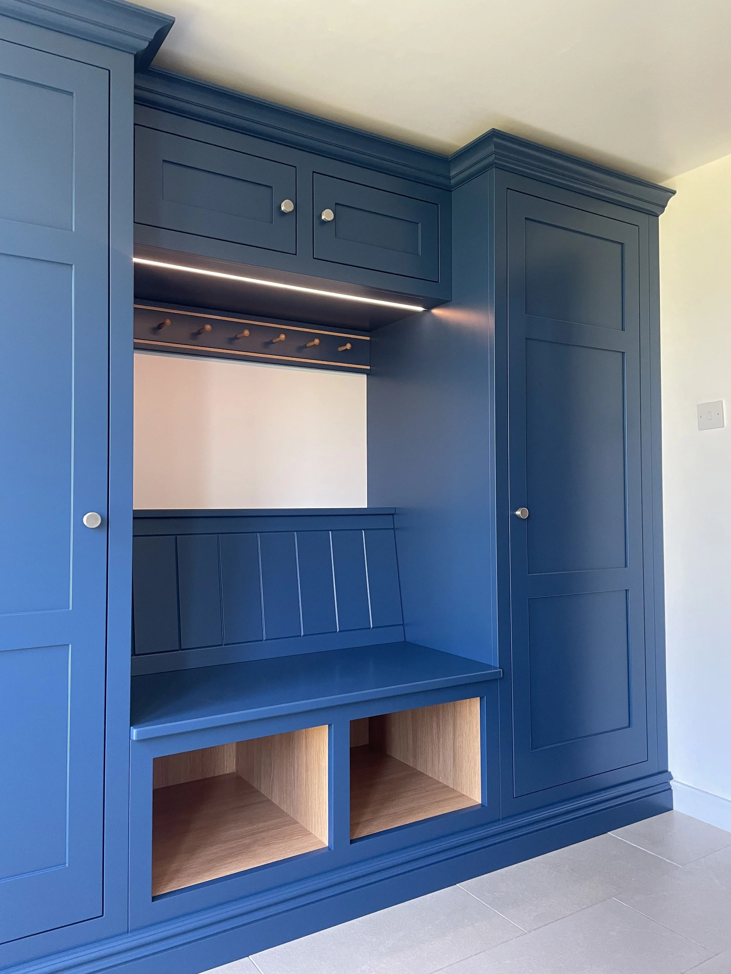 Blue built-in cabinetry with various compartments and open shelves, some with wooden interiors, in a room with gray tiled flooring.