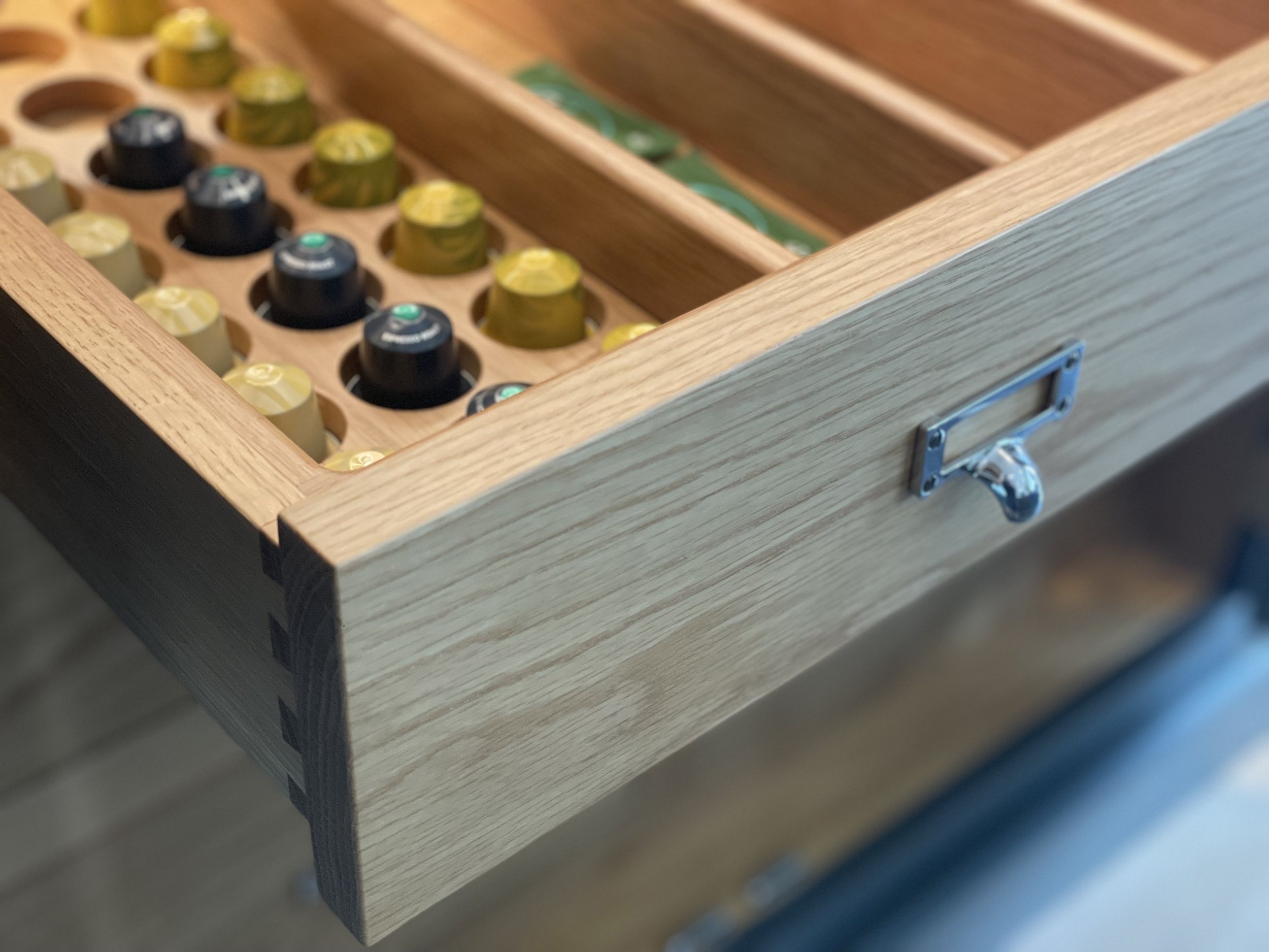 Close-up of a wooden drawer filled with Nespresso capsules, with some capsules in black, green, and beige colors visible.