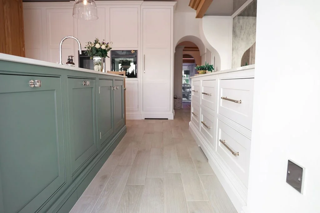 A modern kitchen with a green island and white cabinets, with flowers and decorative items on the counter.