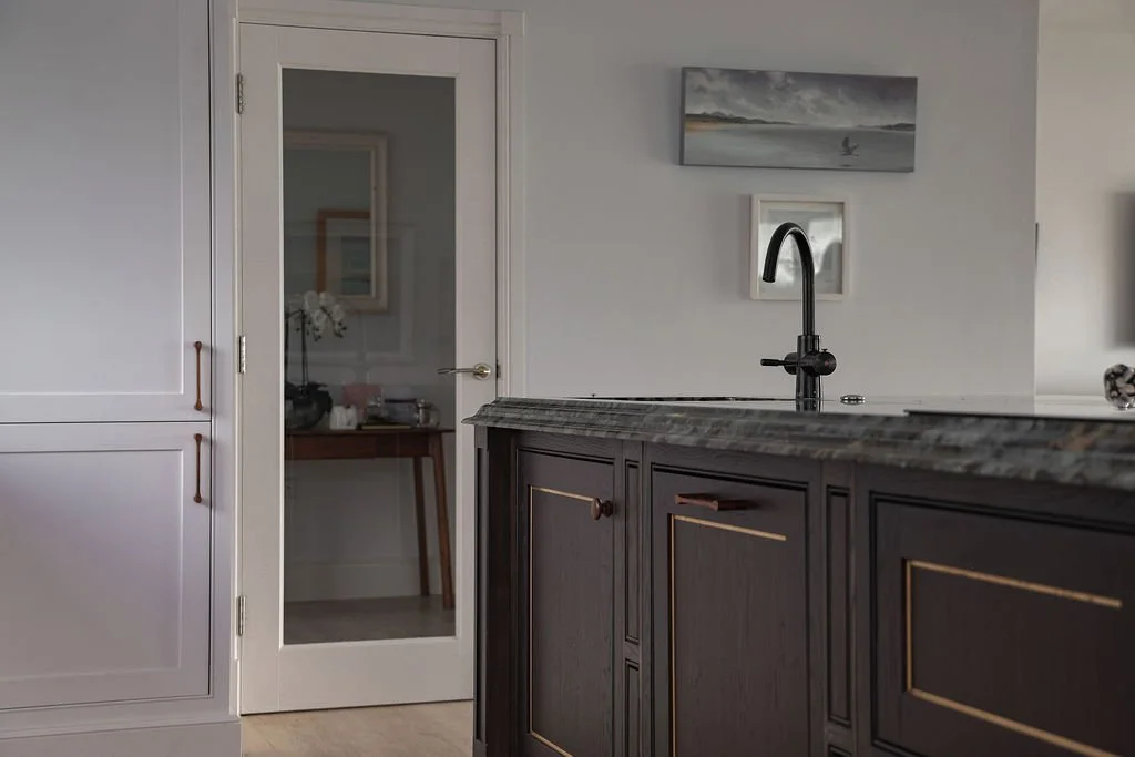 View of a kitchen with a black sink and faucet, dark cabinetry, a door with glass panel, a white wall, and wall art.