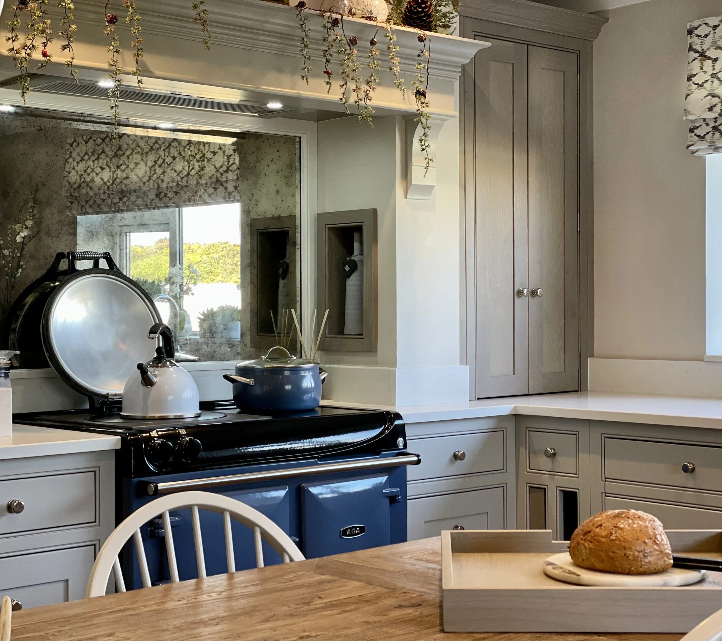 A cozy kitchen with white cabinets, a blue stove, and a round loaf of bread on a wooden tray on a table in the foreground.