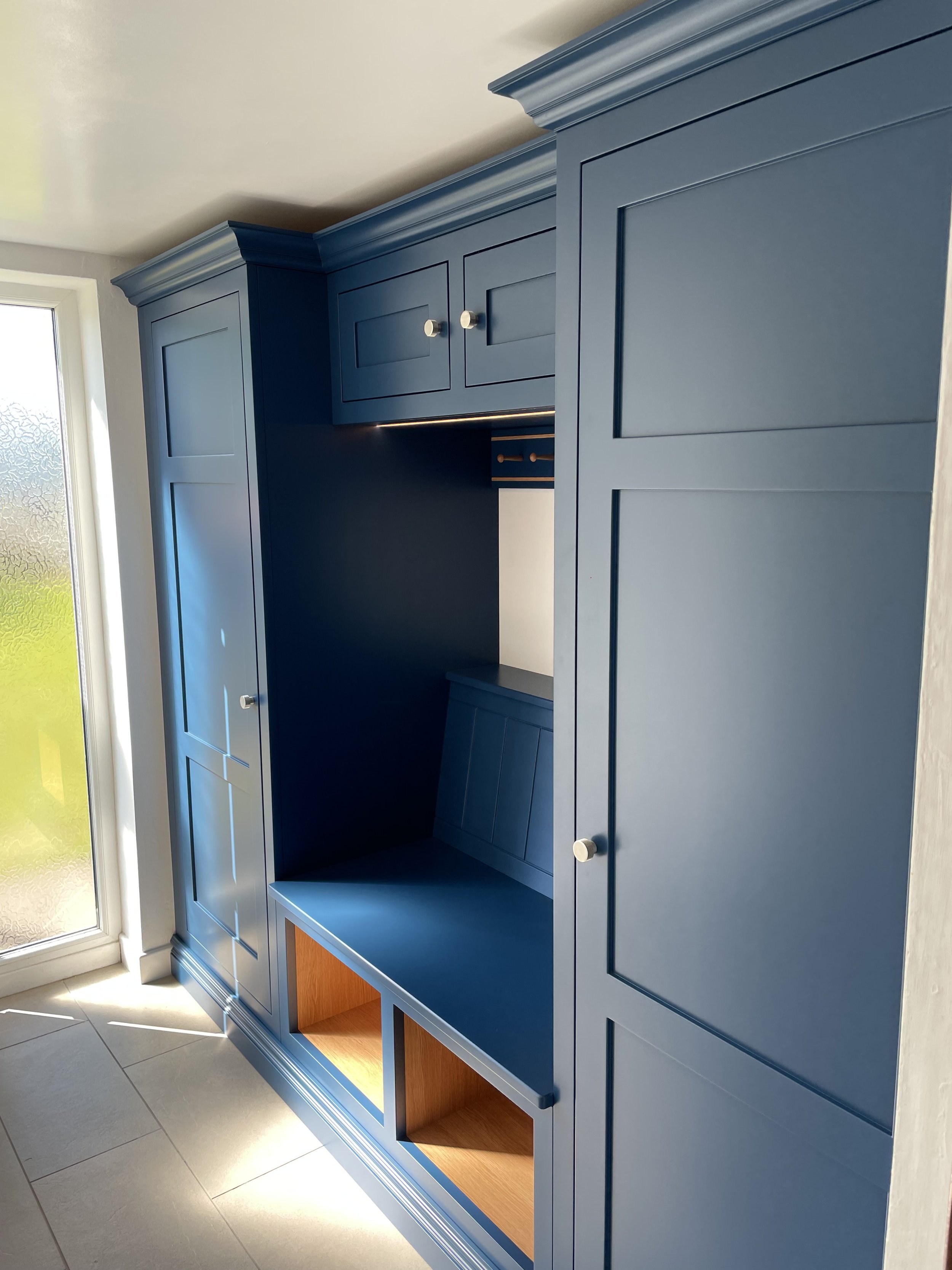 Blue built-in cabinet with closed doors and open shelves near a frosted glass door in a sunlit room.