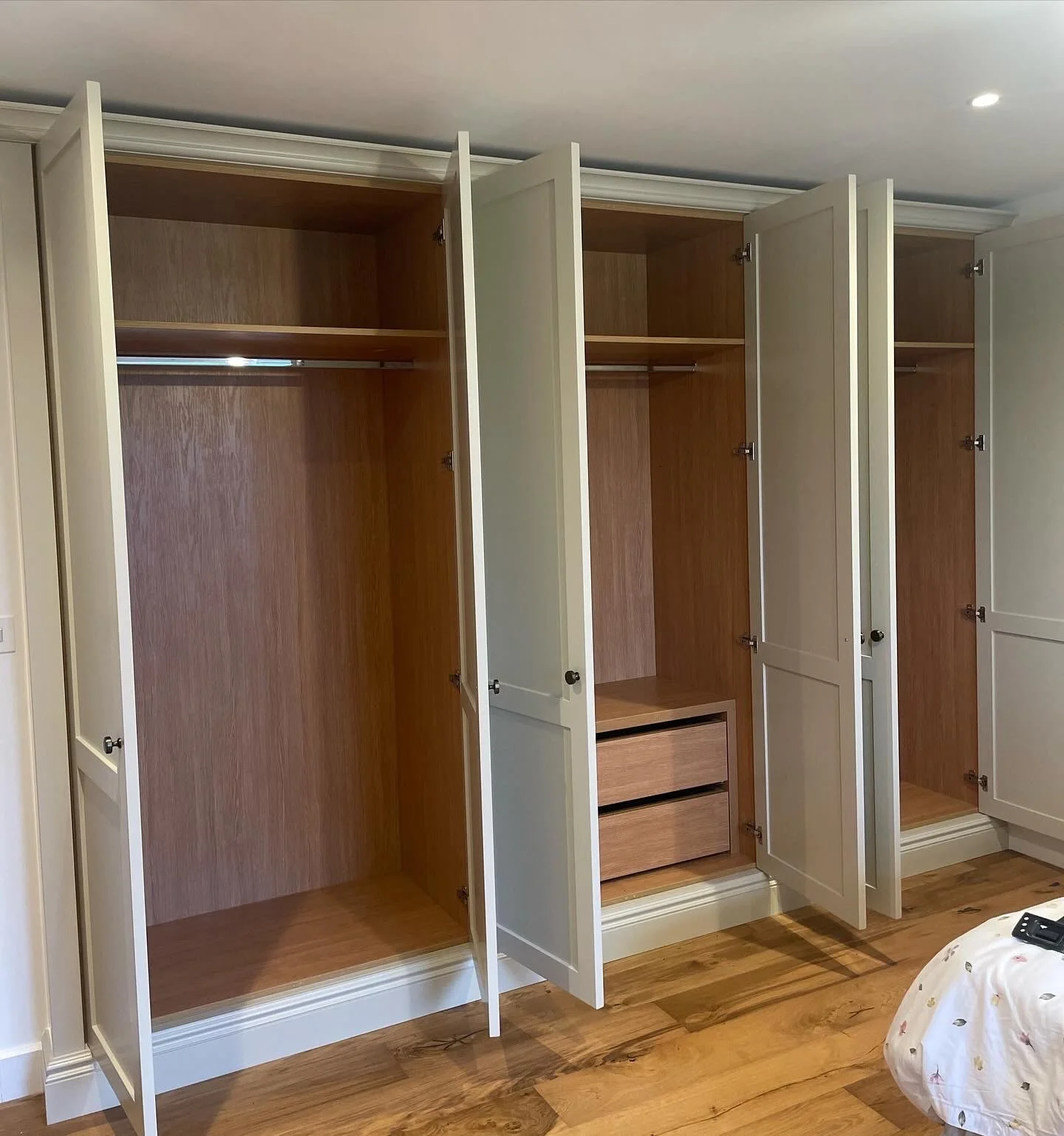 Open empty white wardrobes with wooden interiors and drawers on a wooden floor.