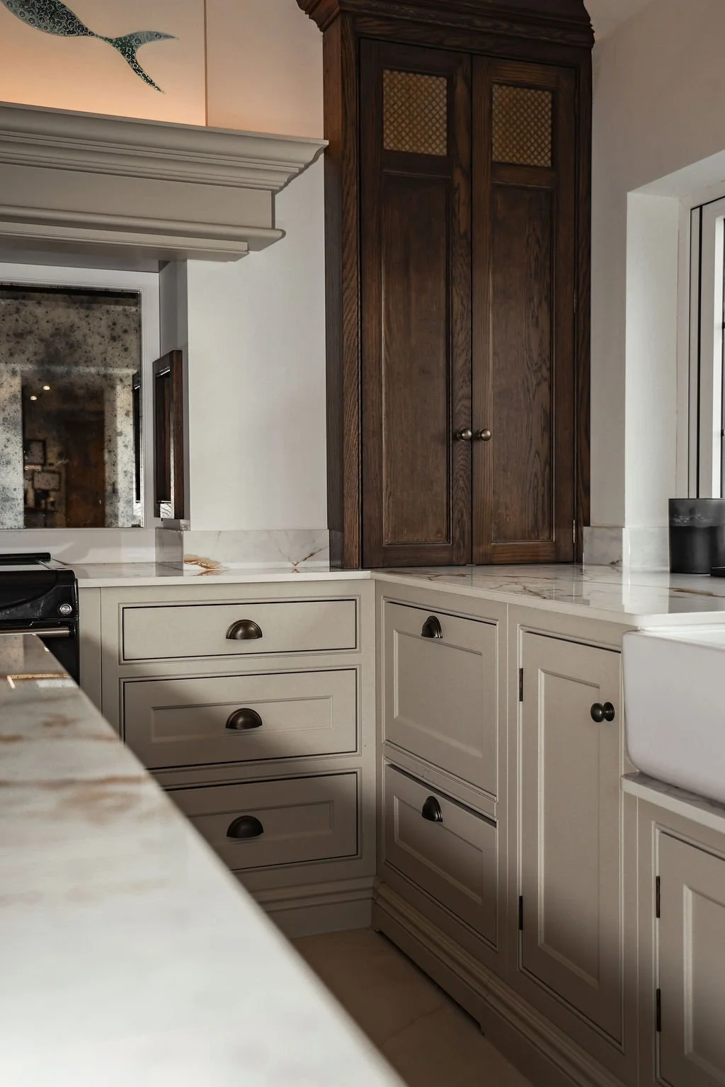 A kitchen corner with white cabinets, a marble countertop, a tall dark wooden cabinet with lattice detail, and a window to the right.