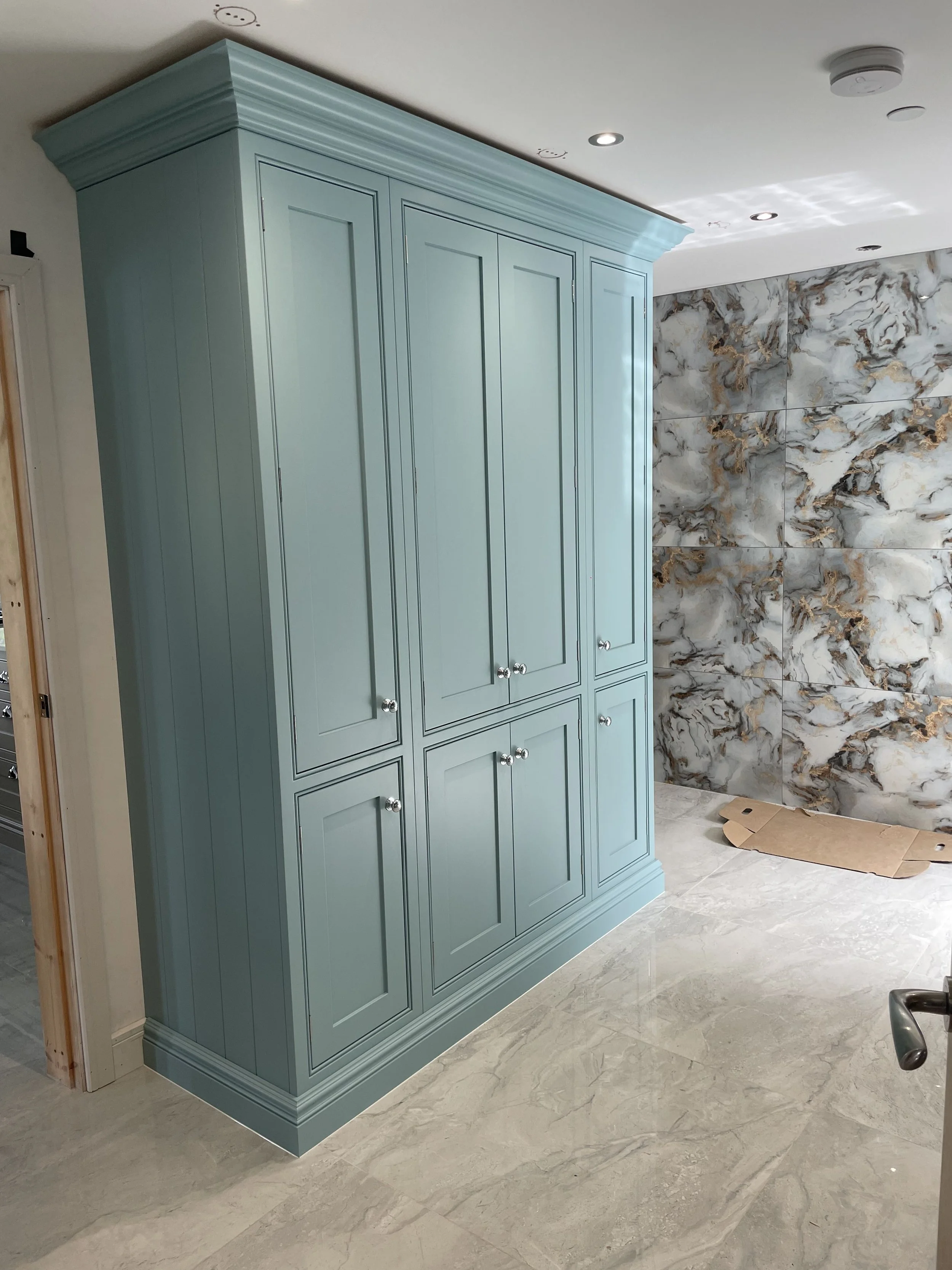 A large, light blue cabinet with silver knobs, situated on a tiled floor with a marble wall in the background.