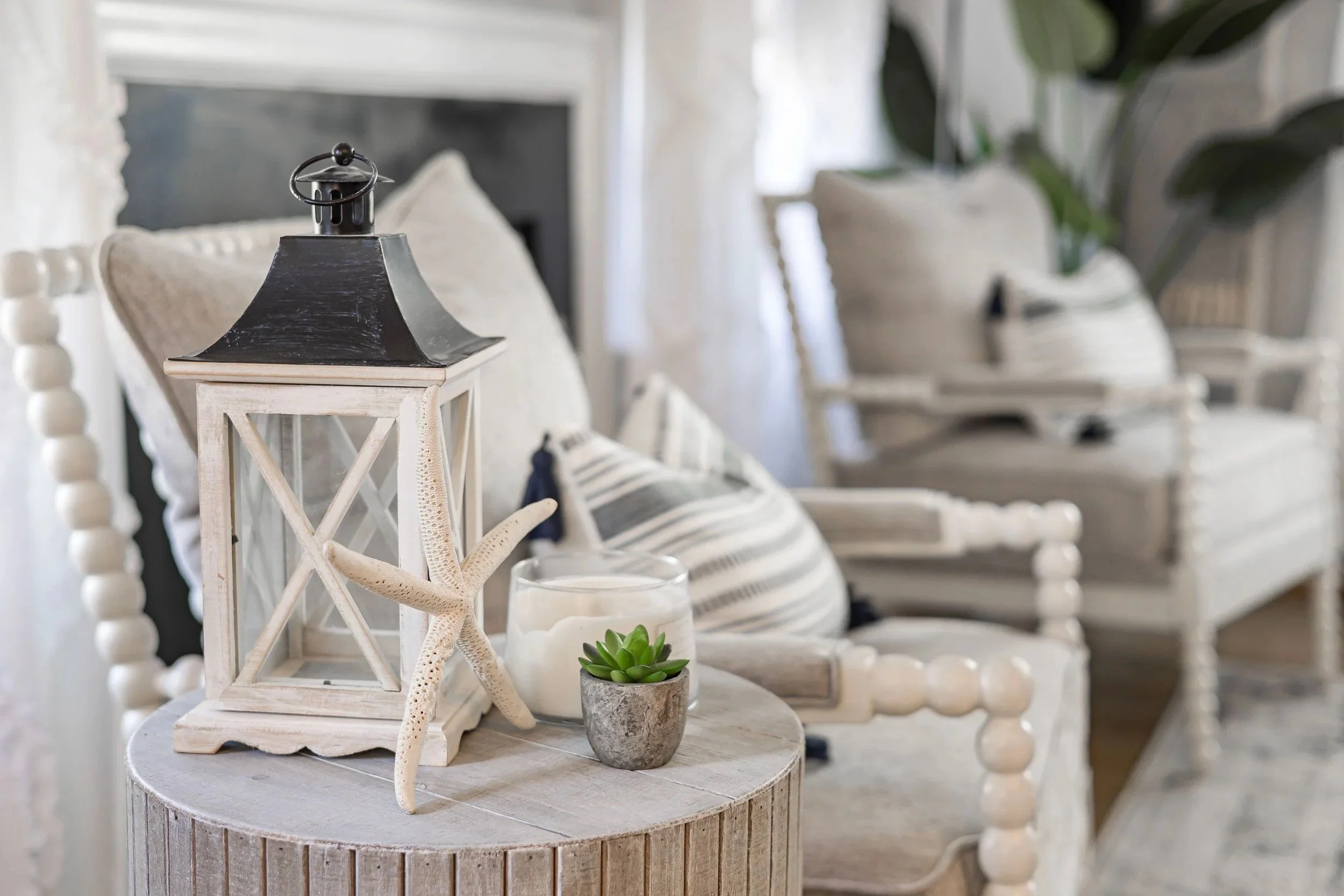 eaceful coastal cottage living room with soft neutral furnishings, weathered wood, lantern, candle, and subtle seaside details.