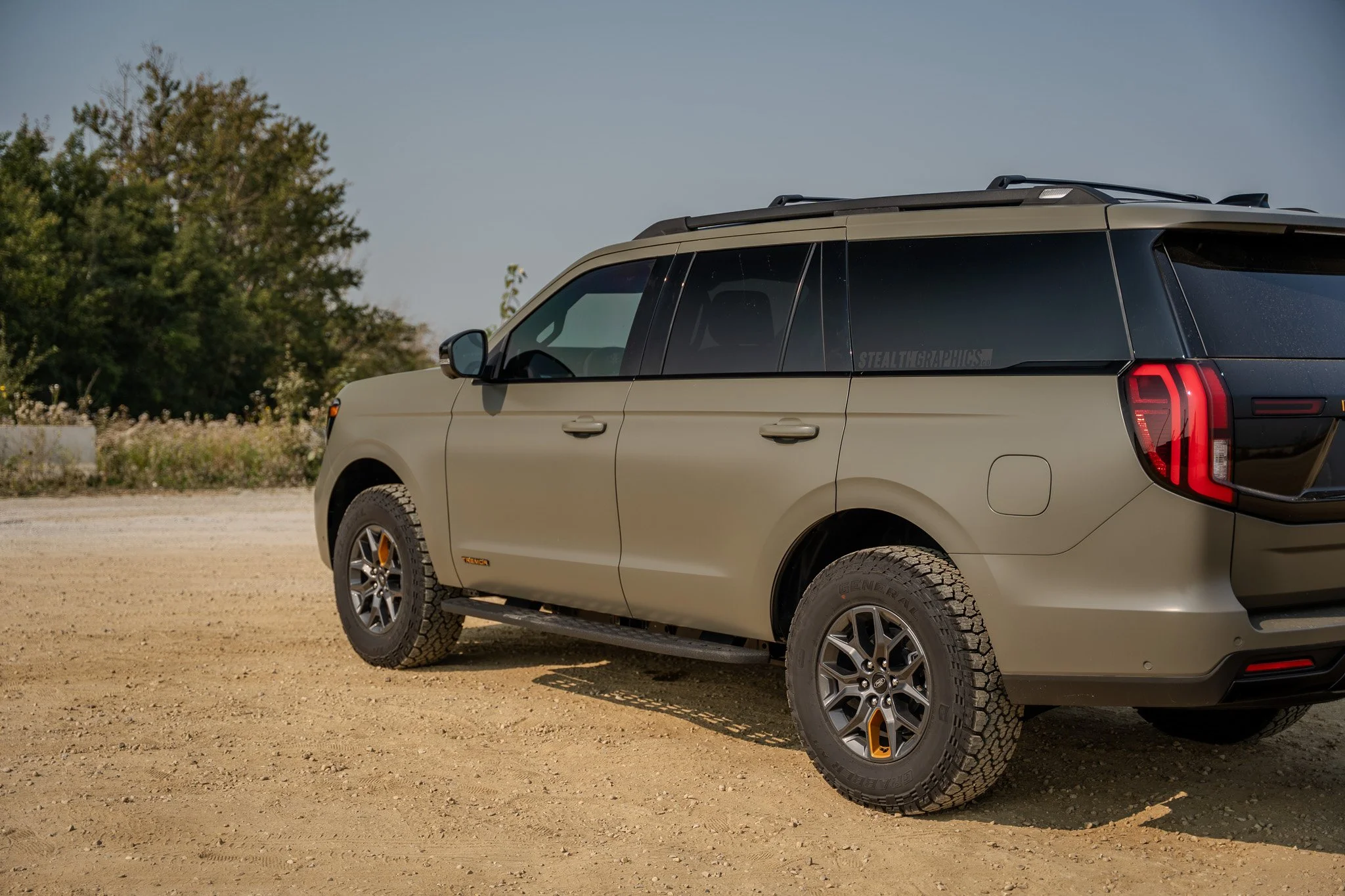 A beige off-road vehicle parked on a dirt surface with trees and bushes in the background. XPEL, 3M, Vinyl, Wraps, Signs