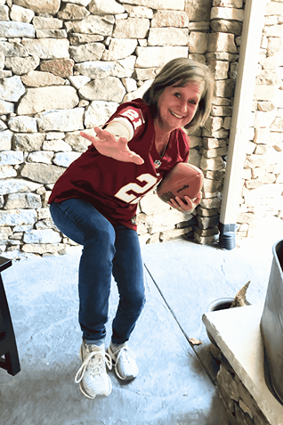 Woman smiling and playfully pretending to throw a football in front of a stone wall
