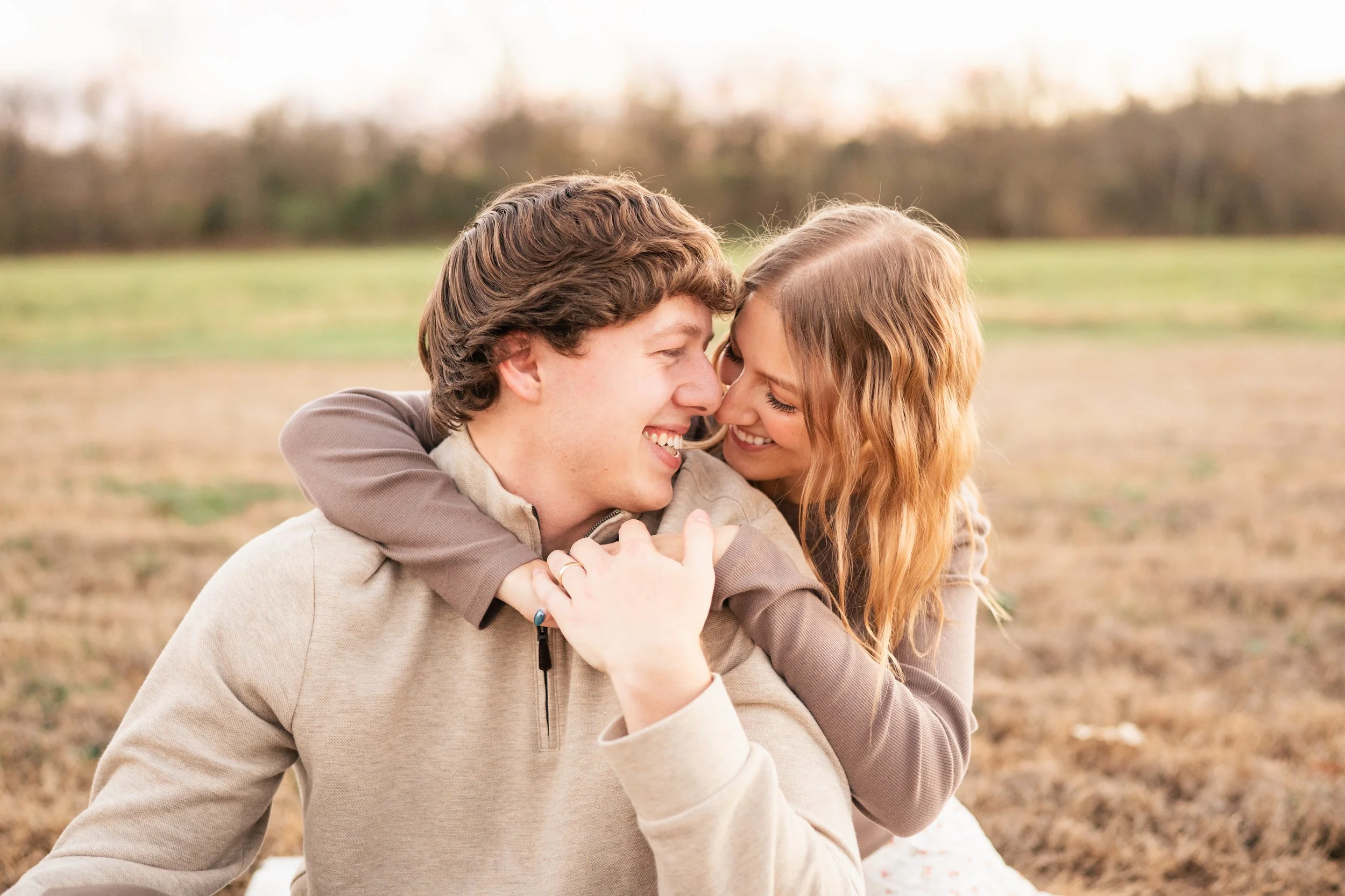 A young couple smiling and embracing each other outdoors in a field with trees in the background