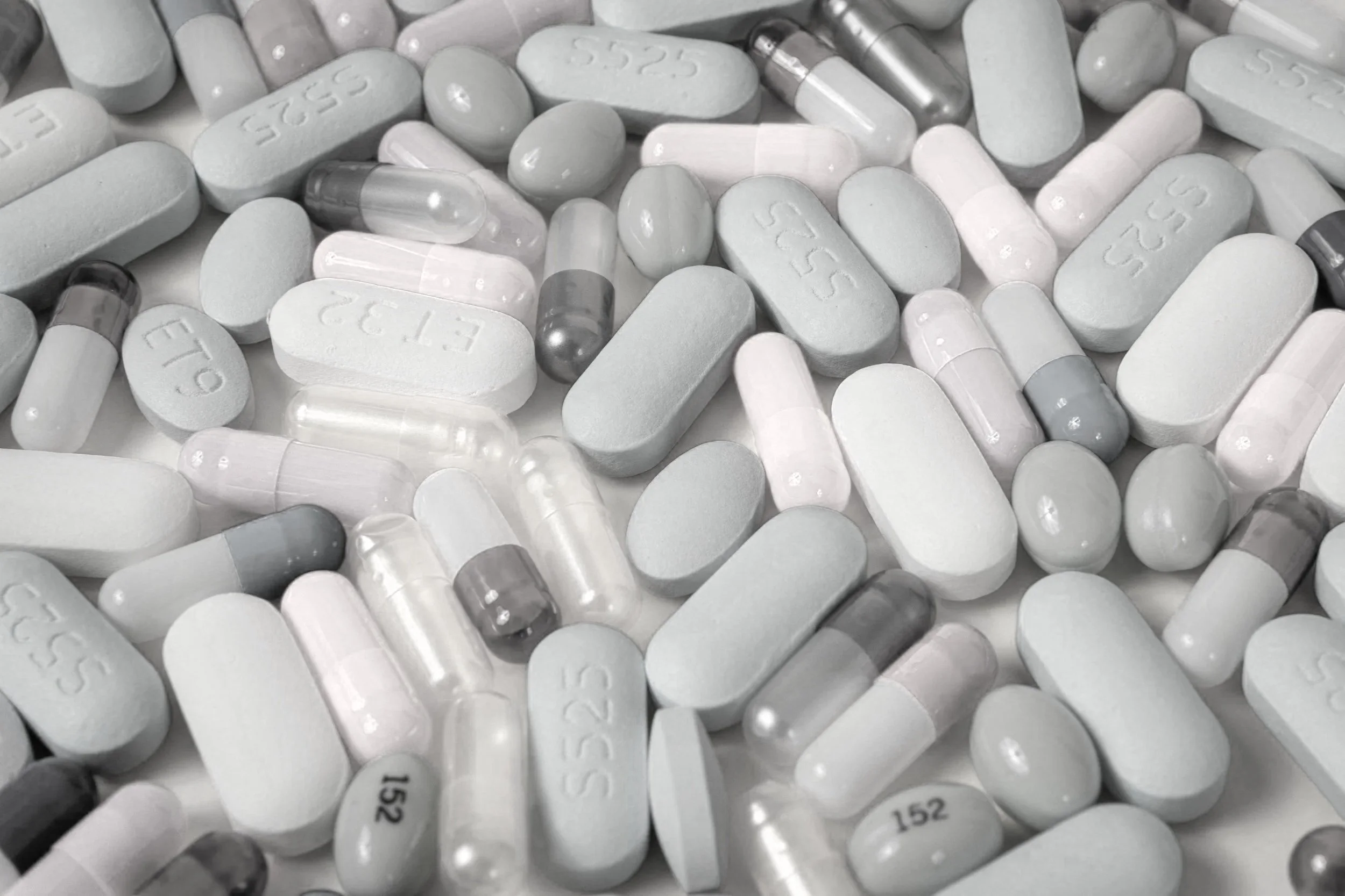 A variety of white pills and capsules, some with imprints and numbers, scattered on a surface.